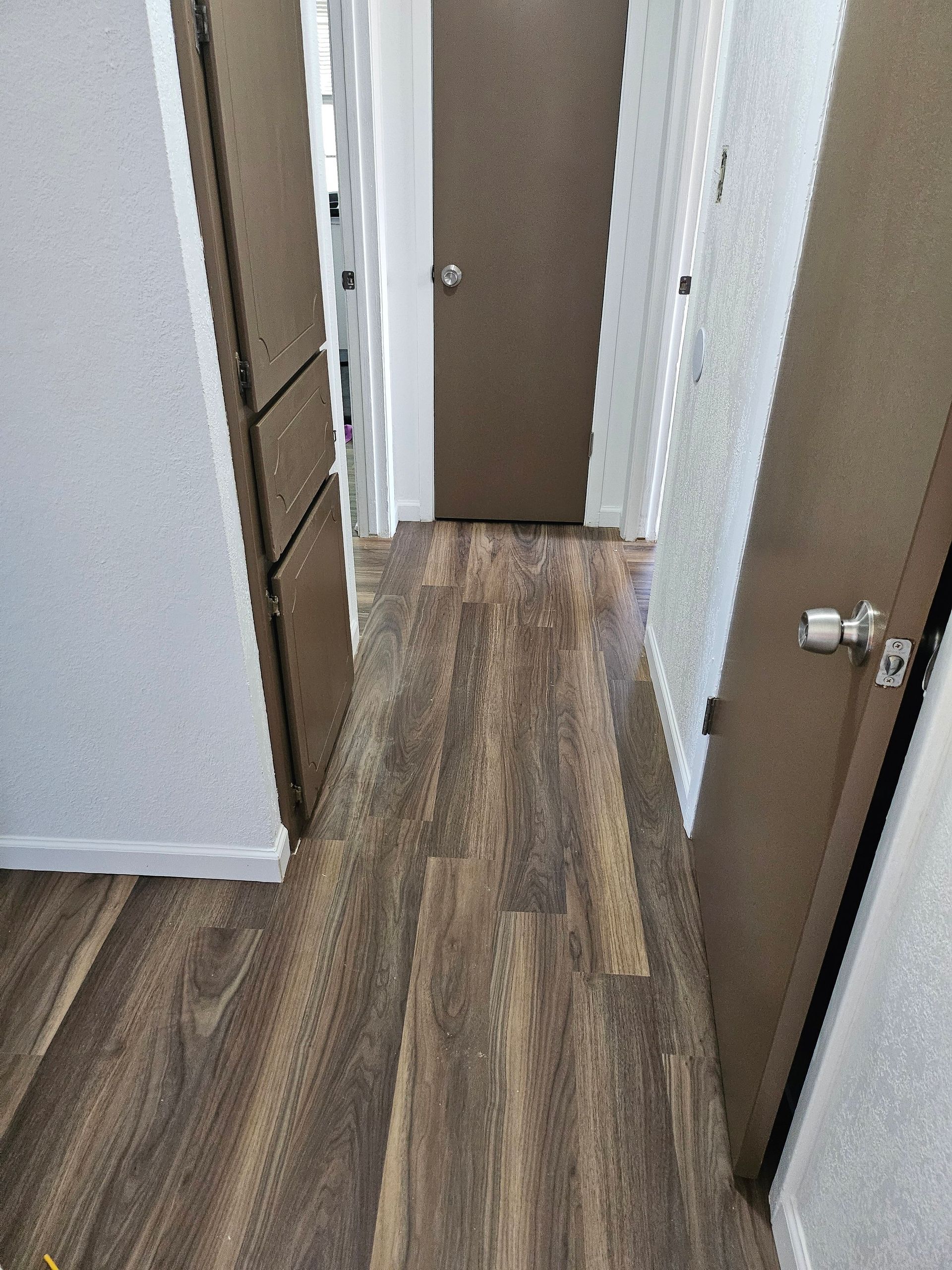 Hallway with brown wood-look flooring, brown doors, and white walls.