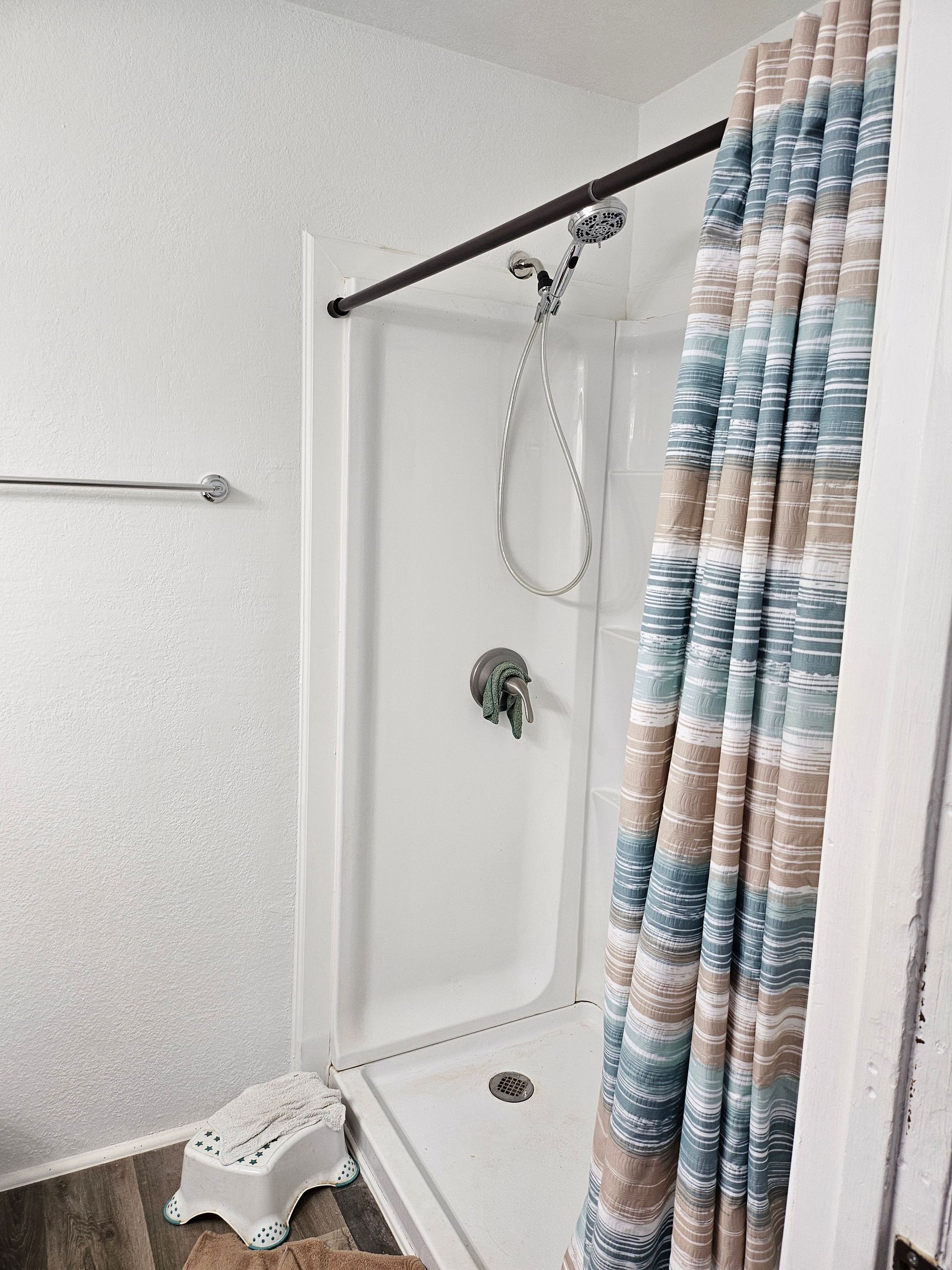 White shower stall with a blue and tan striped shower curtain and a step stool.