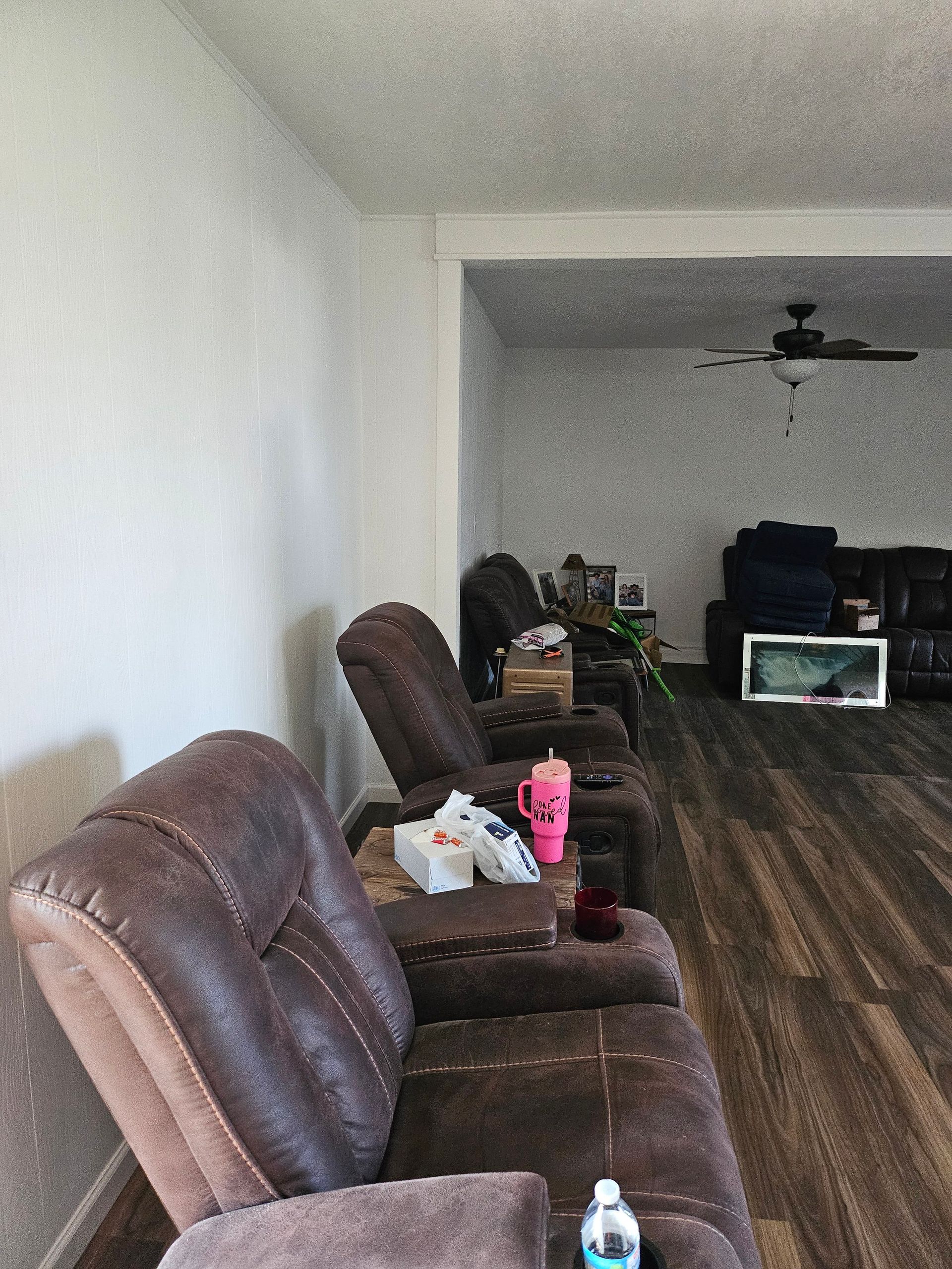Two brown recliners in a living room with wooden floors, a white wall, and a view of a second room.