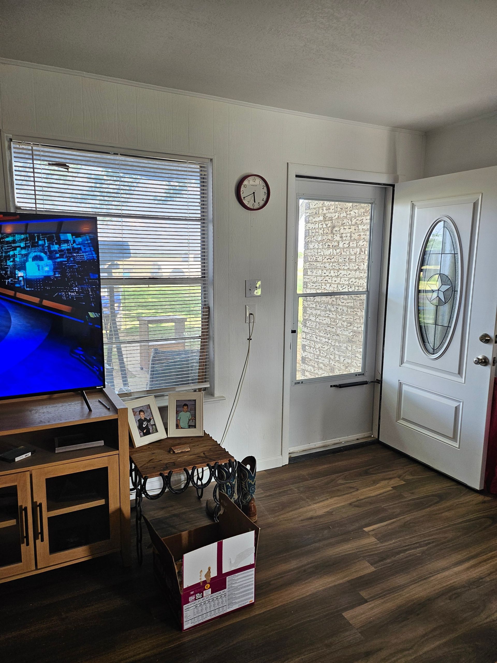 Living room interior with TV, window, door, wooden floor, and a small table.