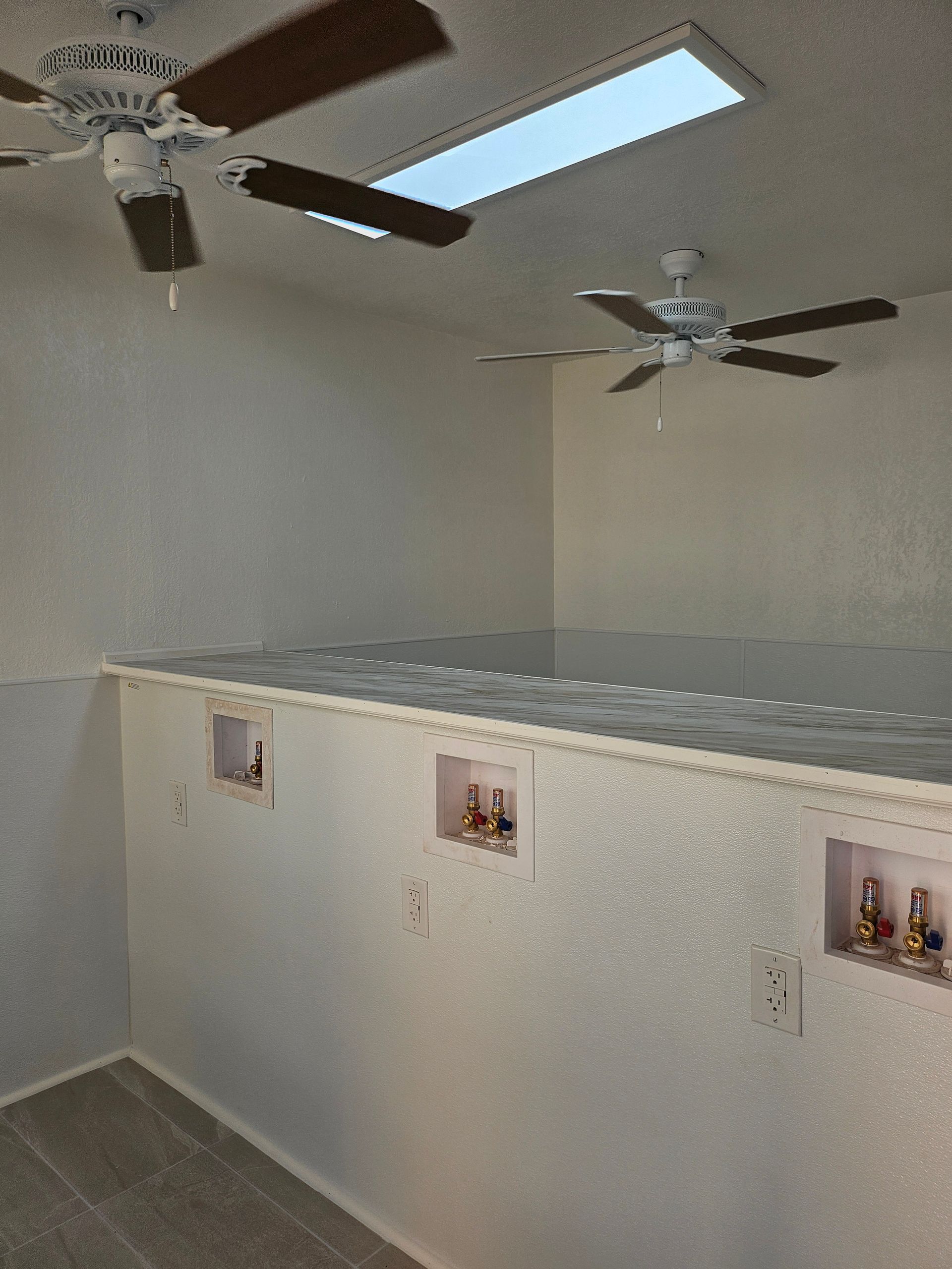 Interior view of a room with two ceiling fans, a skylight, and electrical outlets along a ledge.