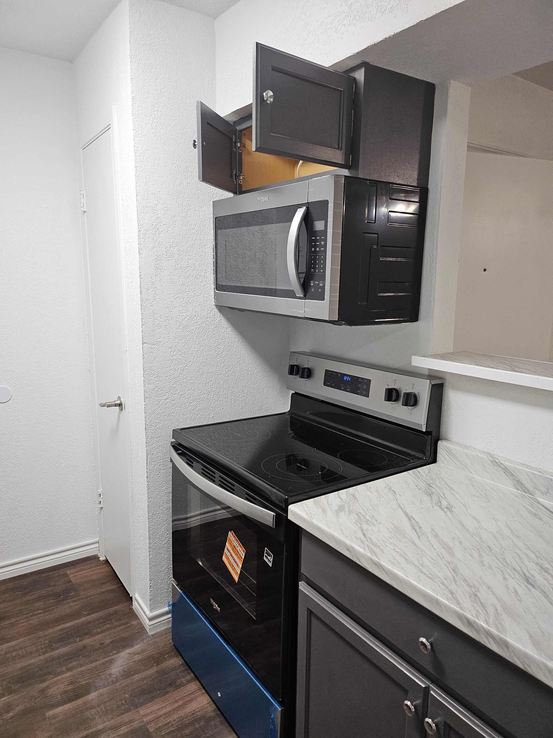 Kitchen with a black stove, microwave, and cabinets. Light gray countertop and patterned wallpaper.