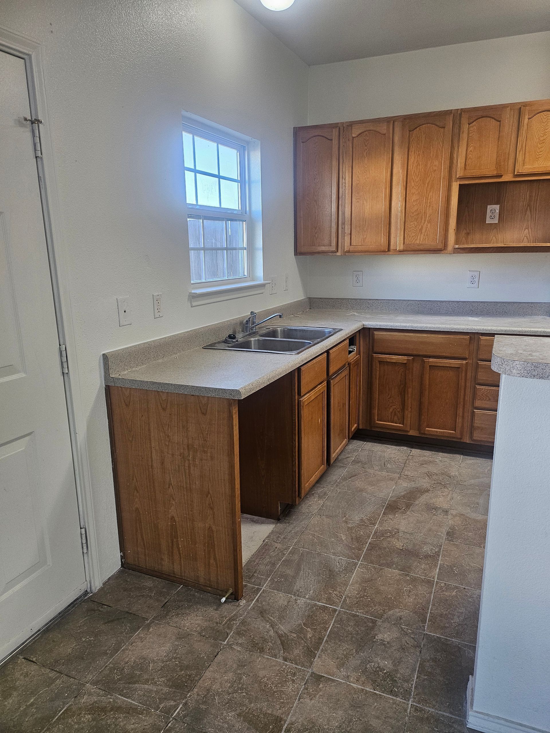 Kitchen with brown cabinets, light countertops, and a window above the sink.