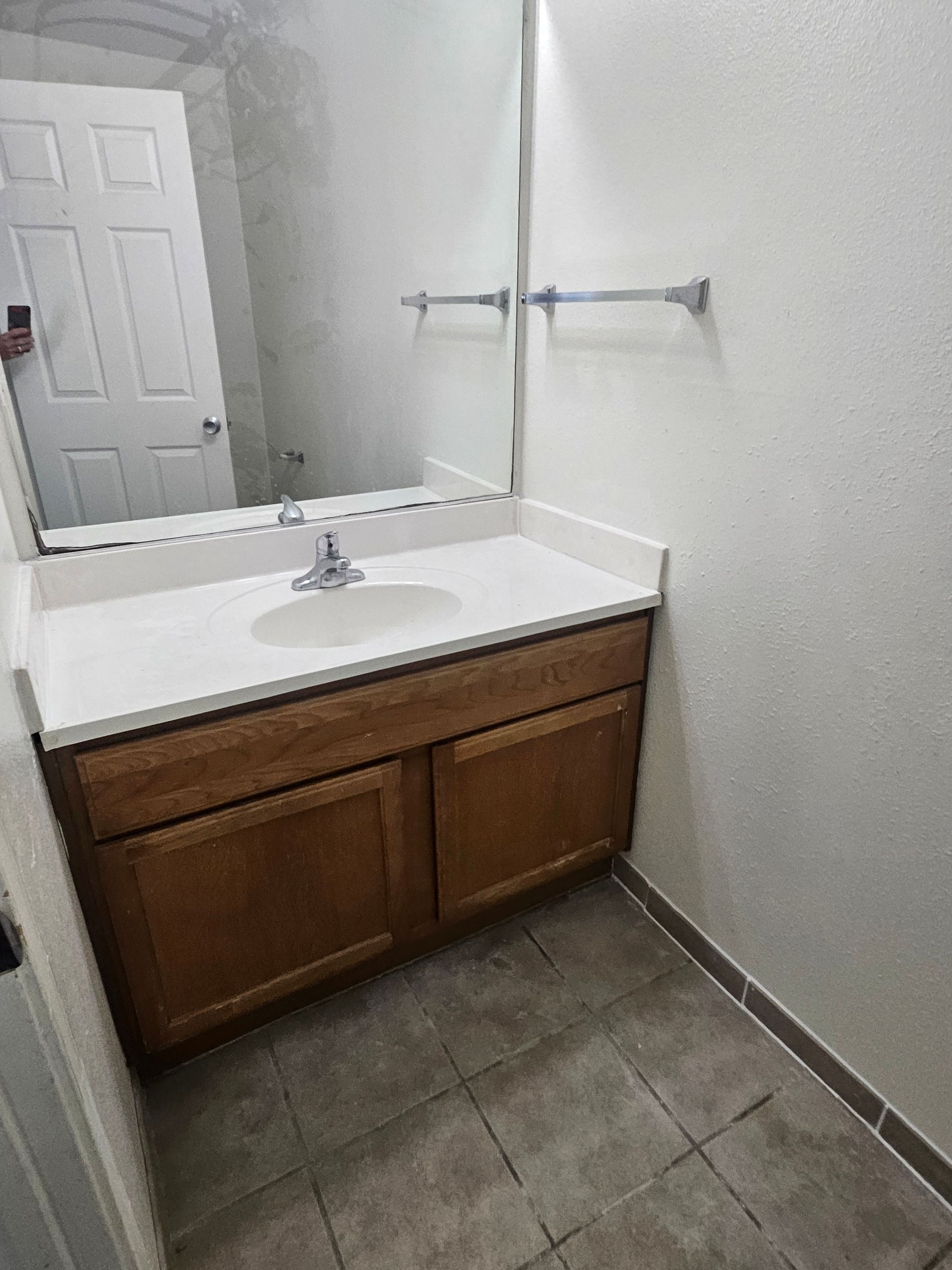 Bathroom with white countertop, brown cabinets, mirror, towel rack, and gray tile floor.