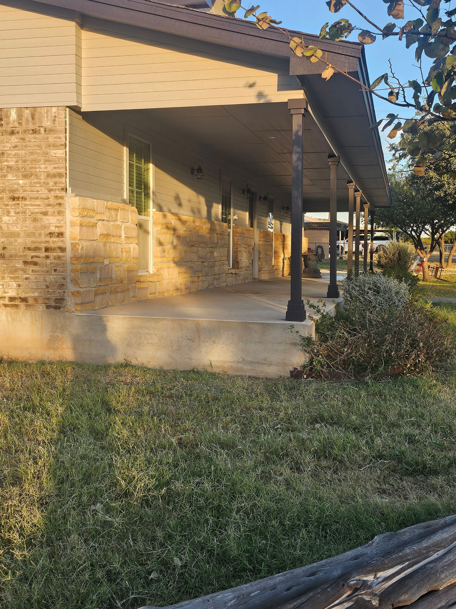 Beige brick and stone building with a long porch, overgrown grass in foreground.