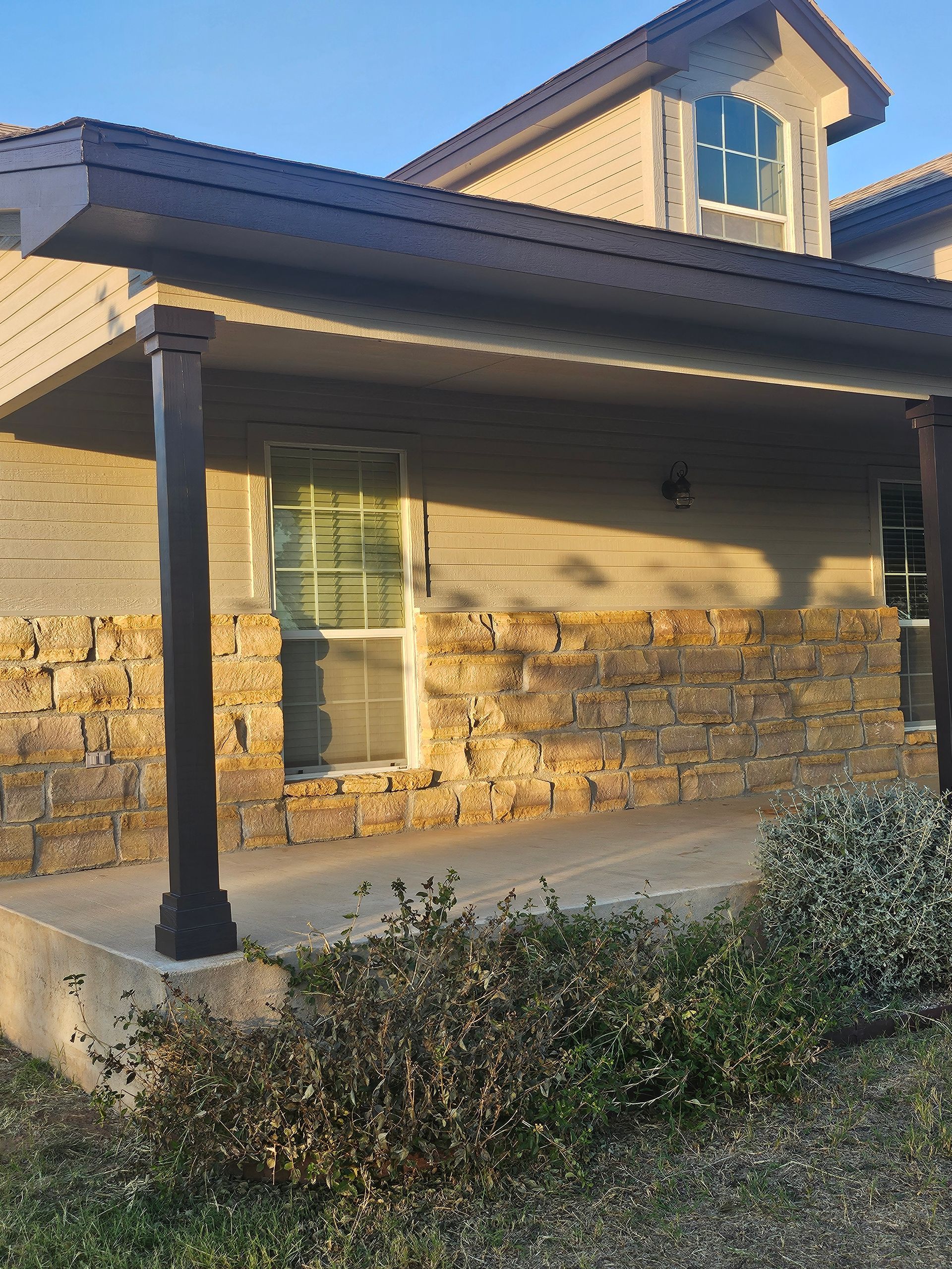 Beige building exterior with stone facade, covered porch, and brown columns.