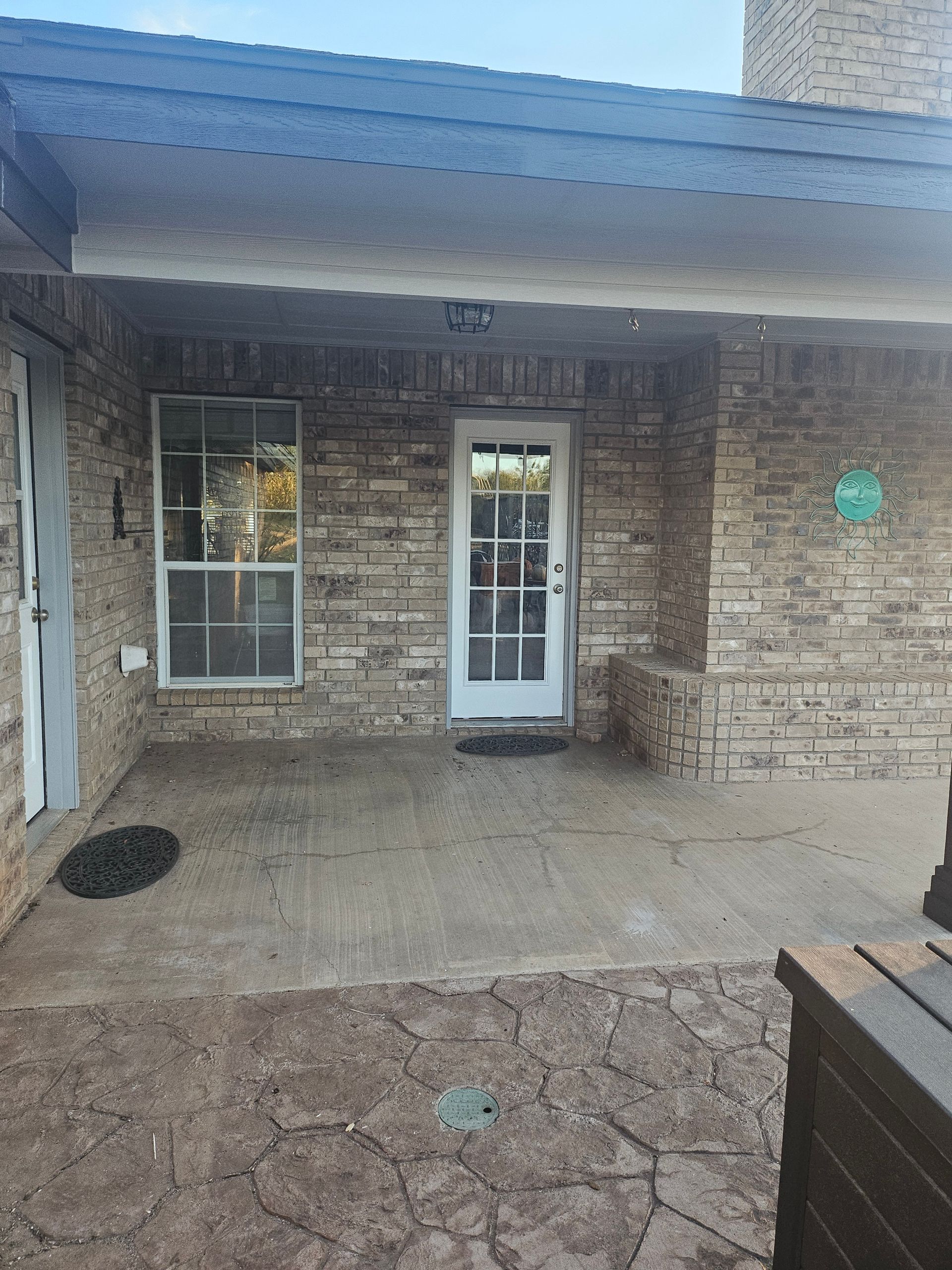 Covered porch with brick facade, a door, and a window. A walkway and a black door mat are visible.
