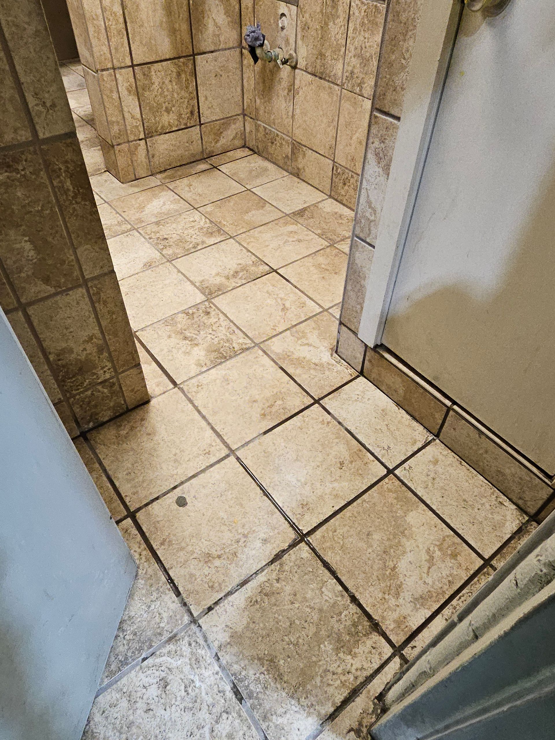 Tiled bathroom floor viewed from doorway; tiles are light brown with dark grout.