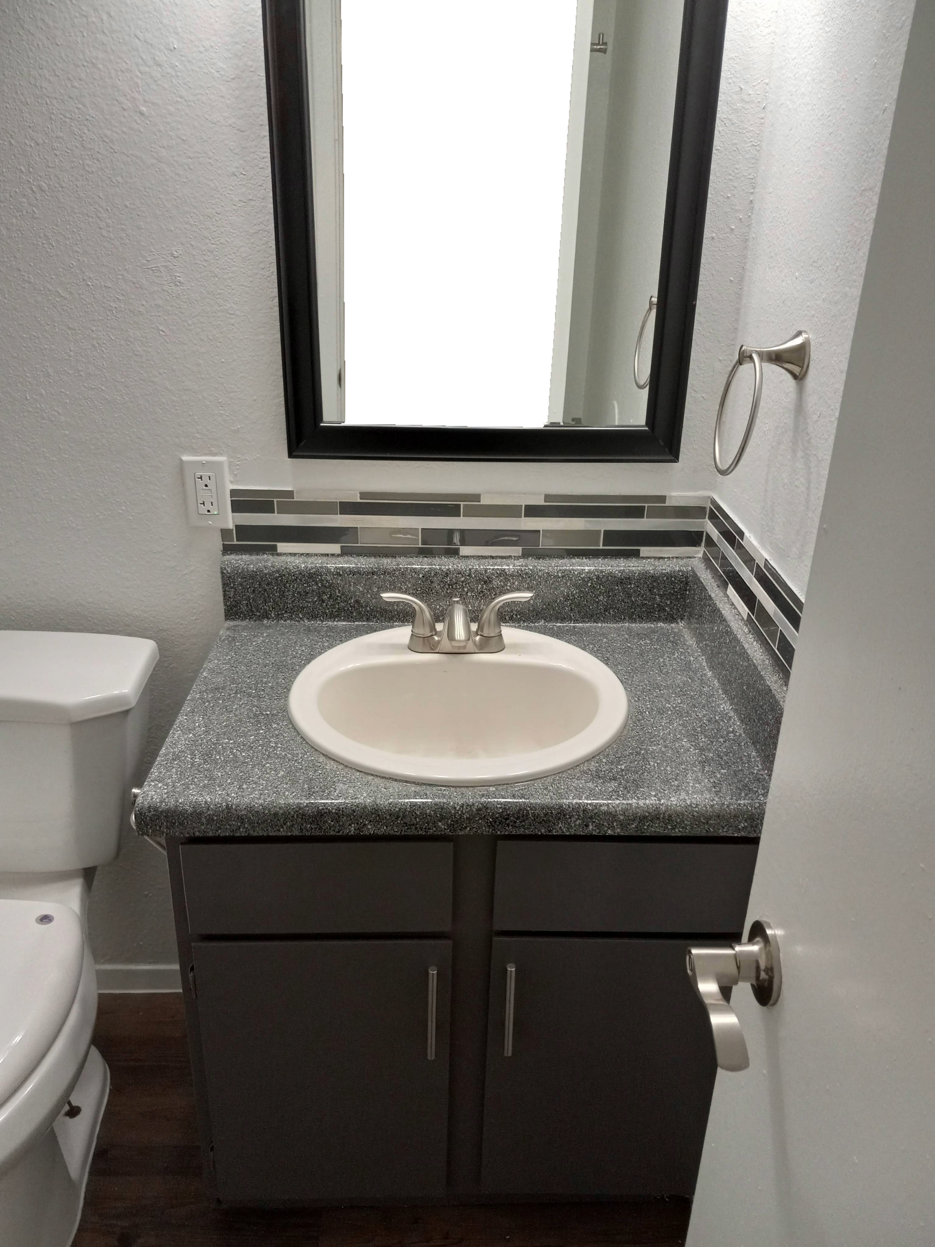 Bathroom with gray vanity, round sink, mirror, and toilet.