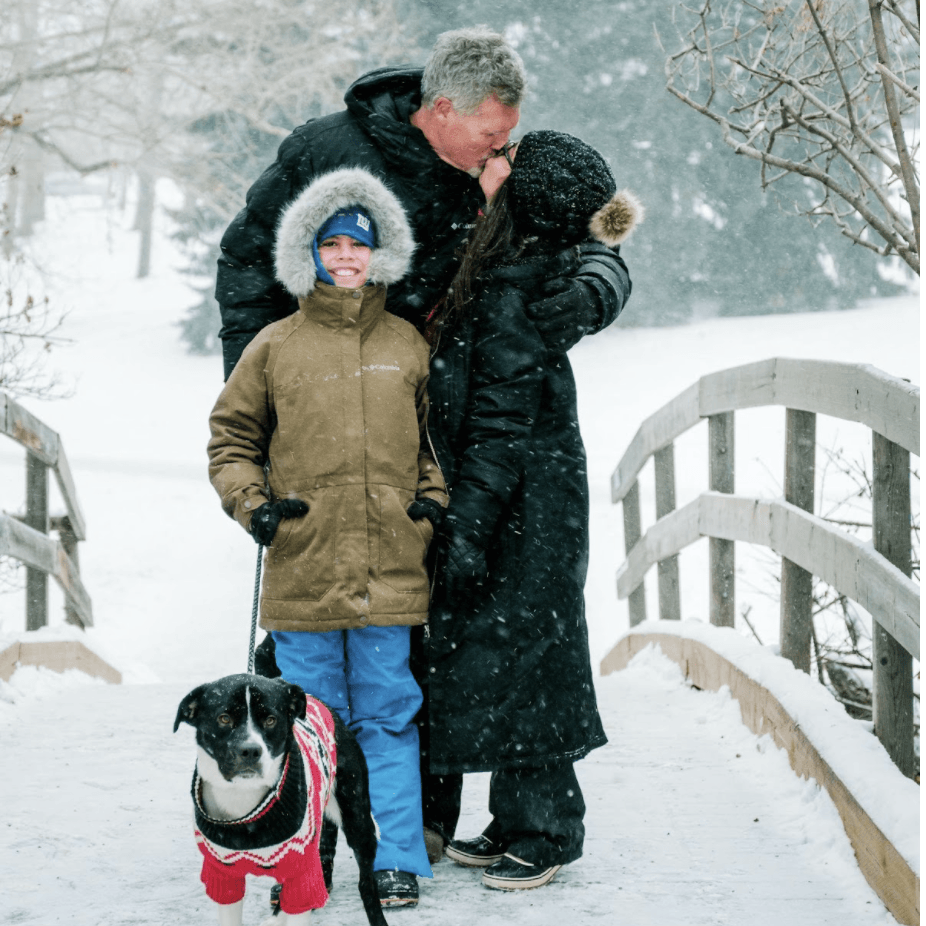 Man kissing woman with a kid and a dog in a park during winter