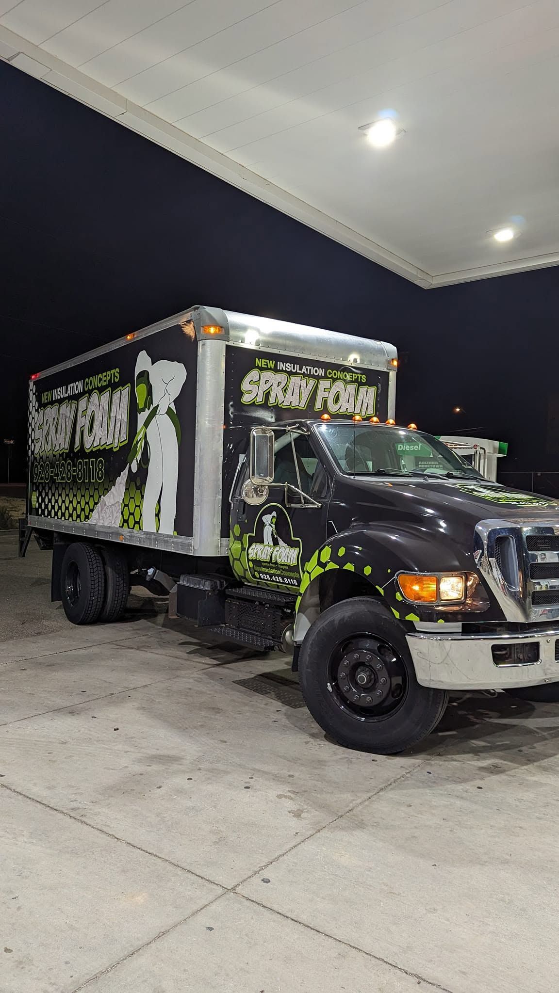 Black box truck with graphics parked under a gas station canopy at night