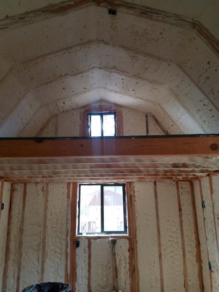 Inside a bare, unfinished room with exposed studs, a sloped ceiling, and two windows.