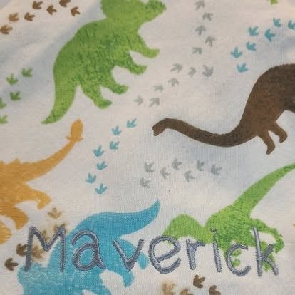 A blanket with dinosaurs and the name maverick embroidered on it