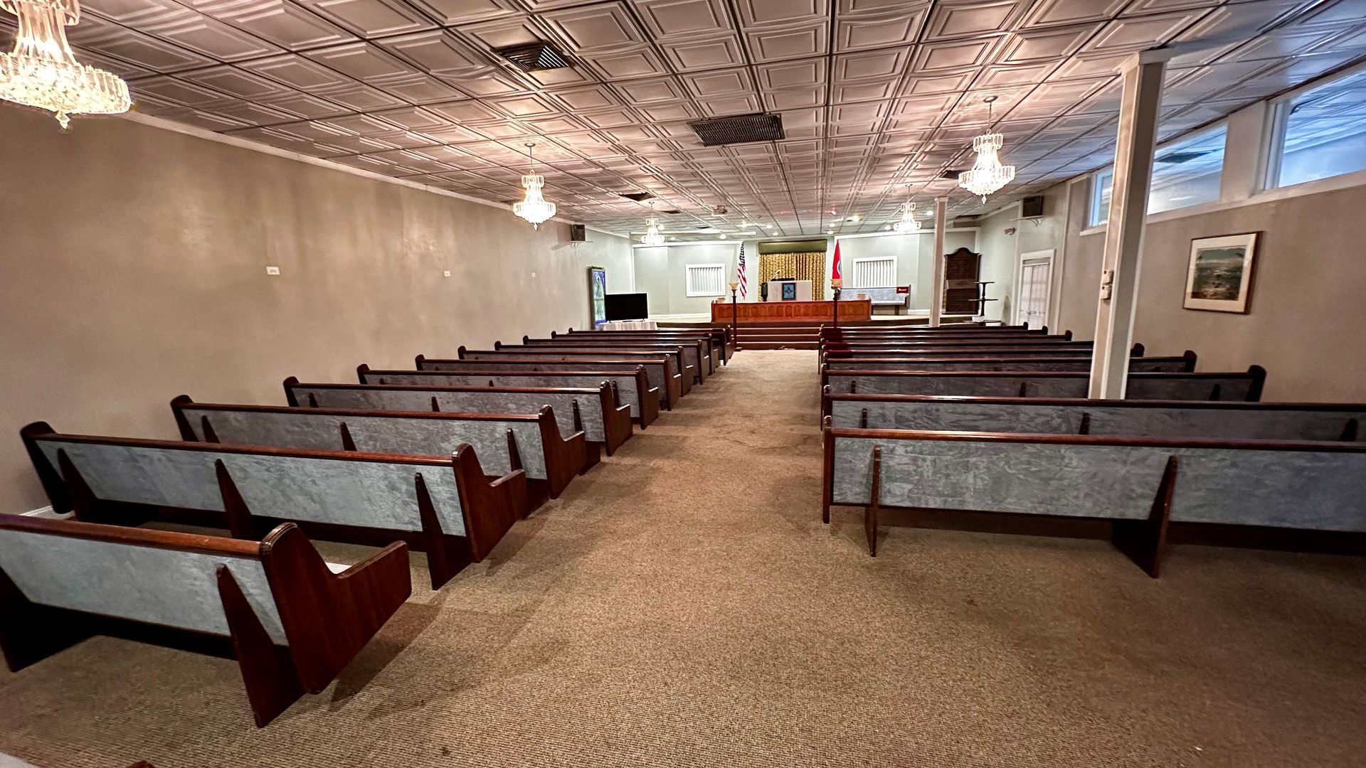 Empty church interior with wooden pews, red carpet, and a white altar at the front.