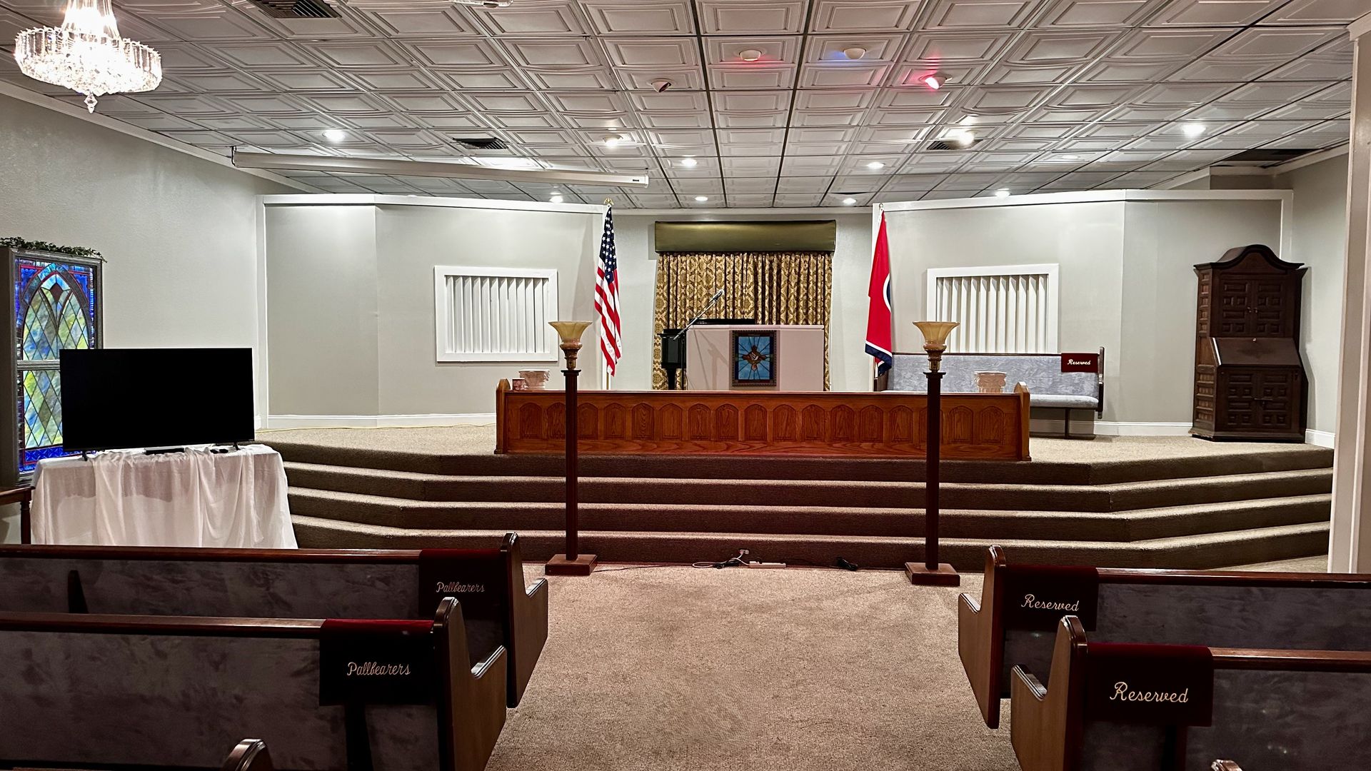Empty courtroom with bench, witness stand, counsel tables, and American and state flags at the front.