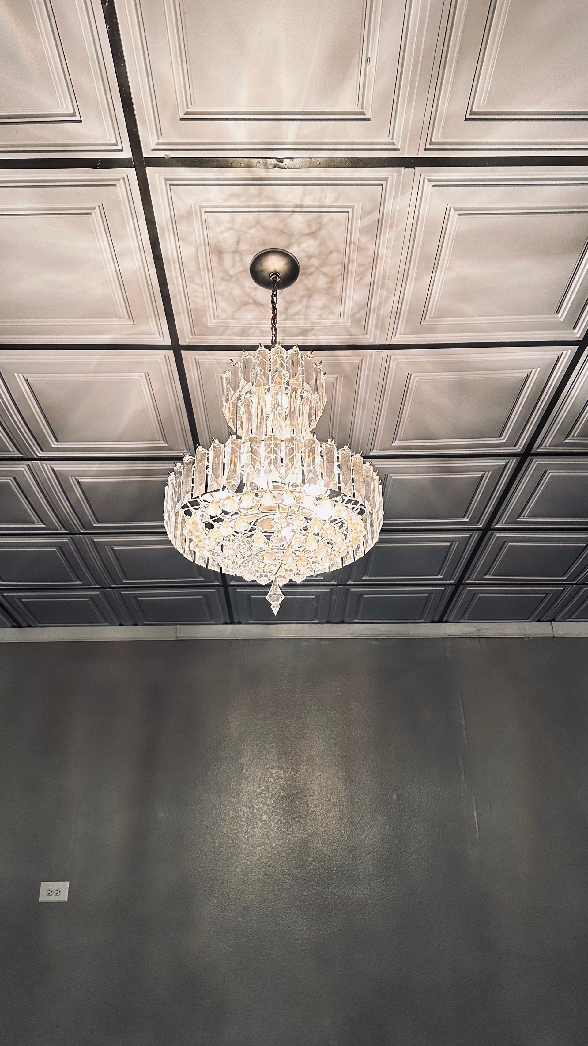 Crystal chandelier hanging from a decorative ceiling in a dark gray room