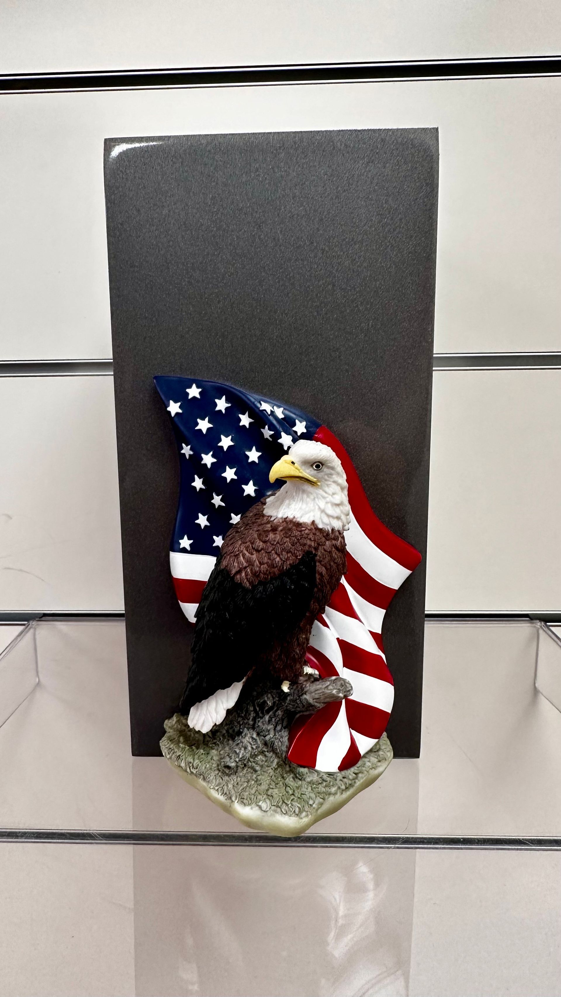 Eagle figurine in front of an American flag backdrop on a gray pedestal