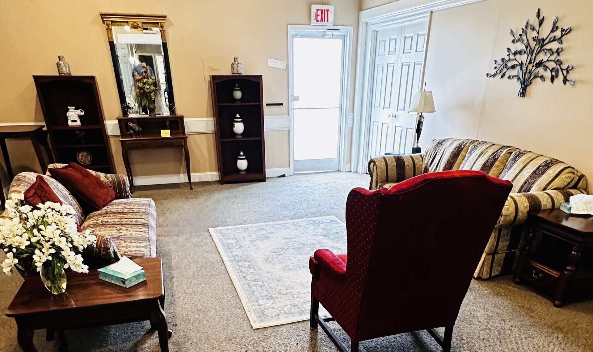 Cozy living room with sofas, red armchair, coffee table, lamp, fireplace mantel, and open door to hallway