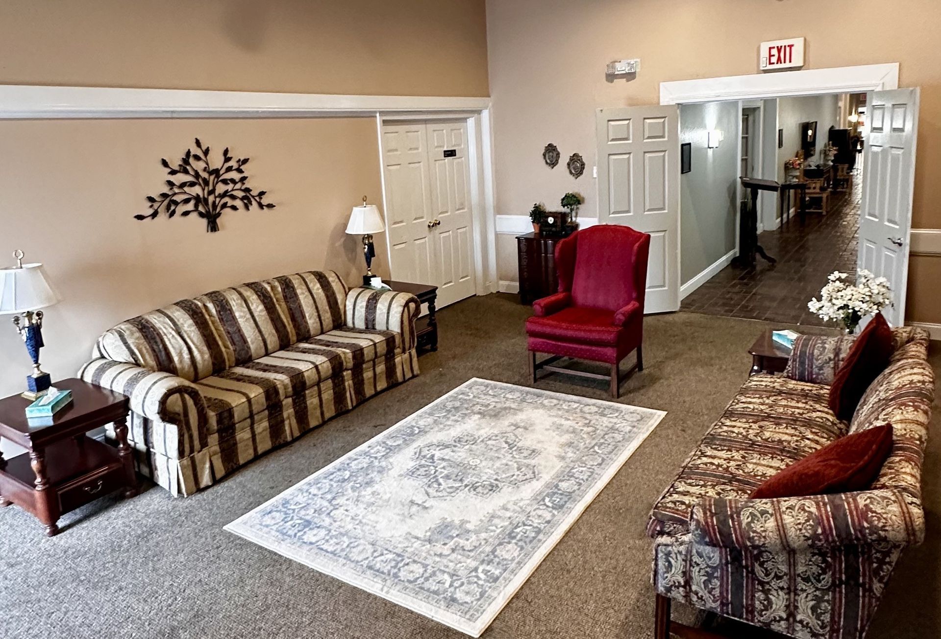 Waiting room with striped and patterned sofas, red chair, rug, and hallway entrance.