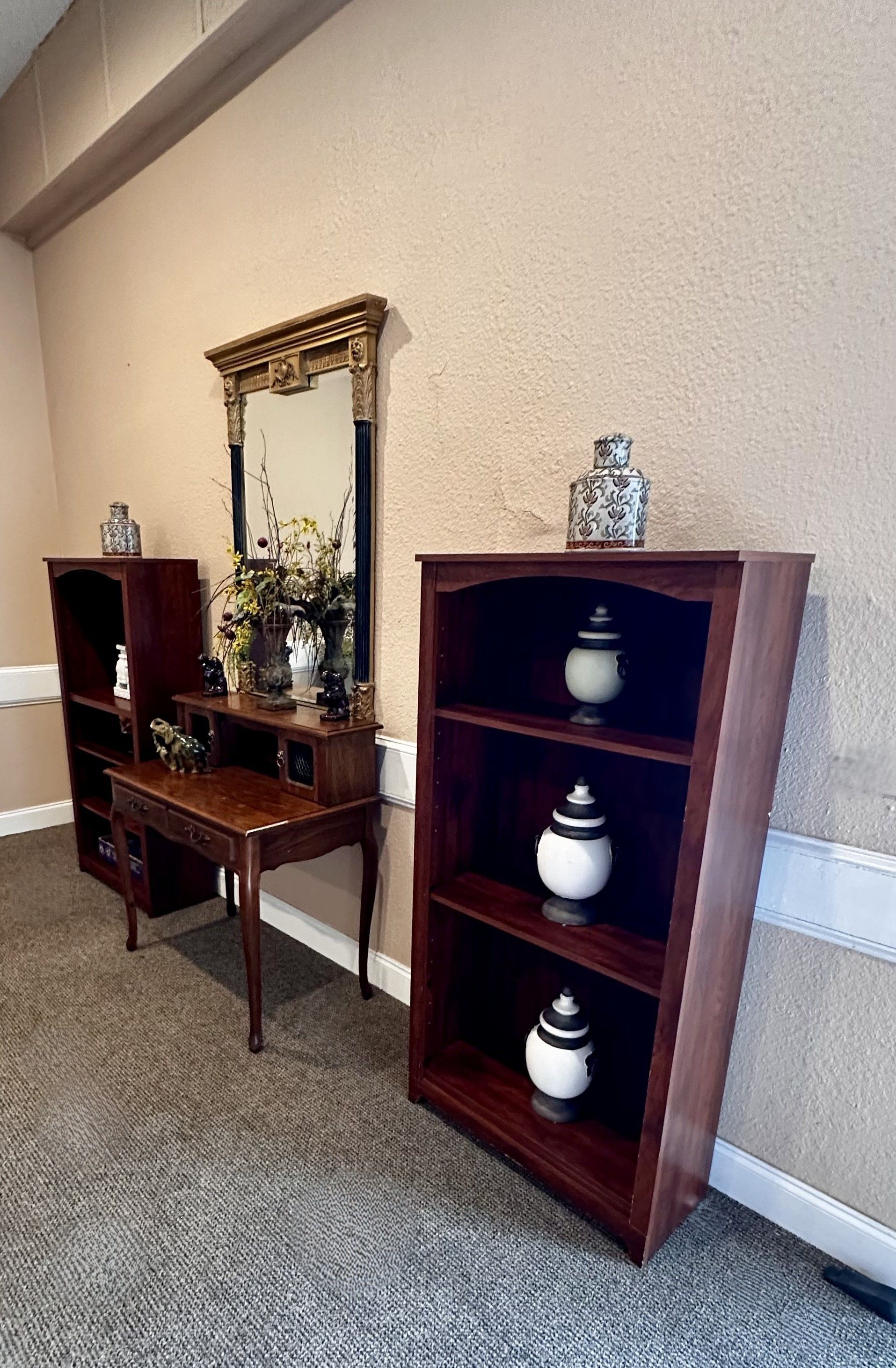 Hallway with wooden shelving, a small vanity table, a mirror, and decorative vases along a carpeted wall