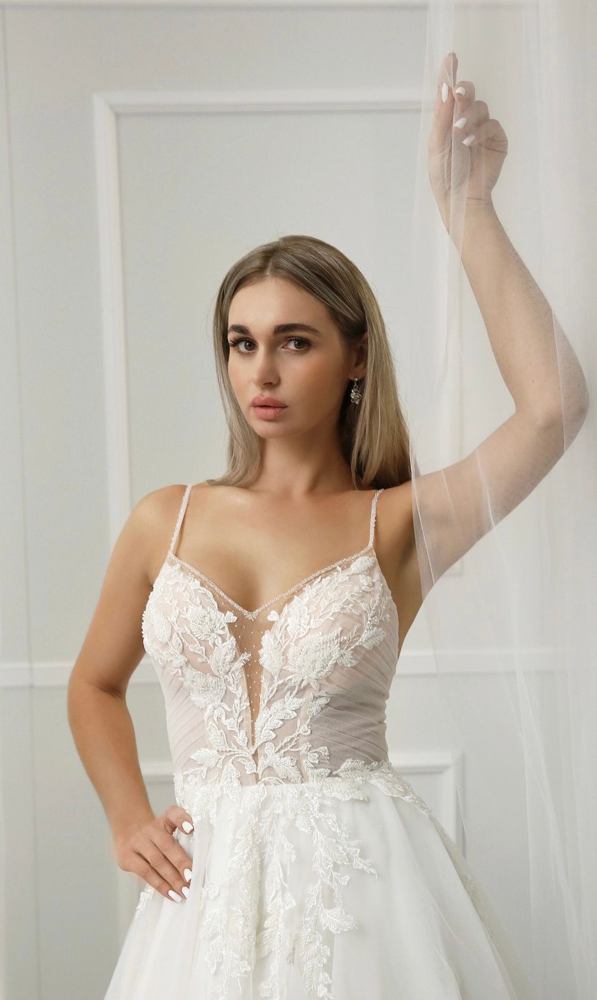 Eine Frau in einem weißen Brautkleid steht vor einem Fenster.