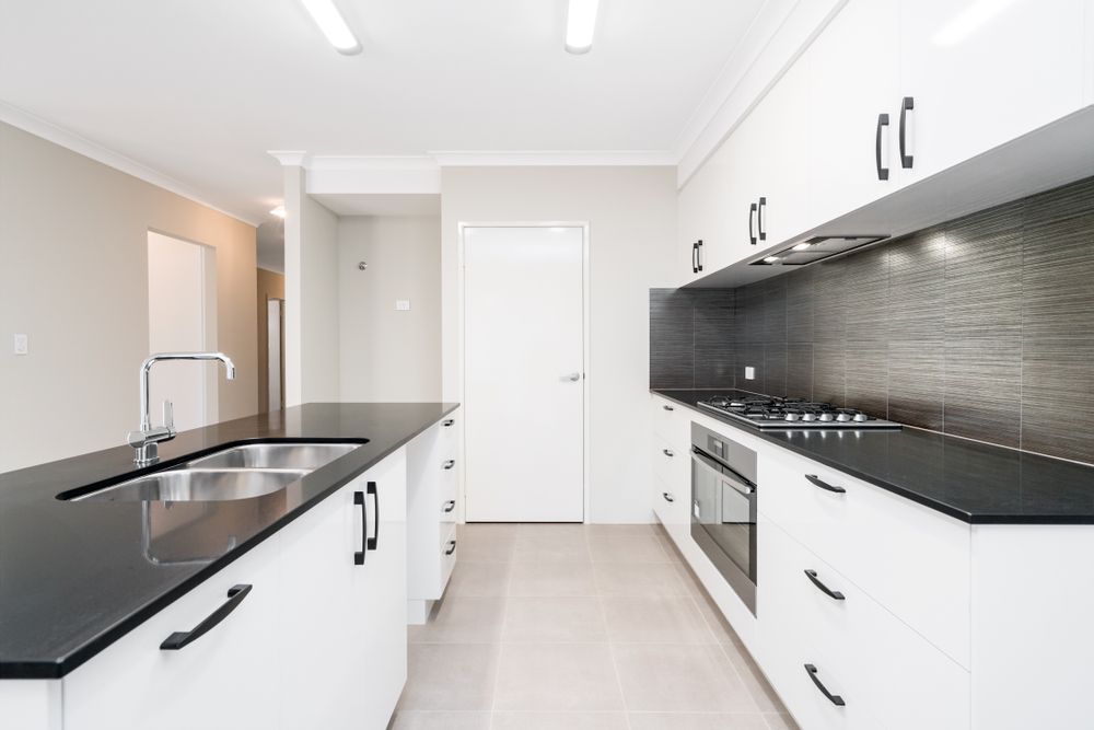 An Empty Kitchen With Black Counter Tops and White Cabinets — Bathurst Bathroom Solutions In Eglinton, NSW