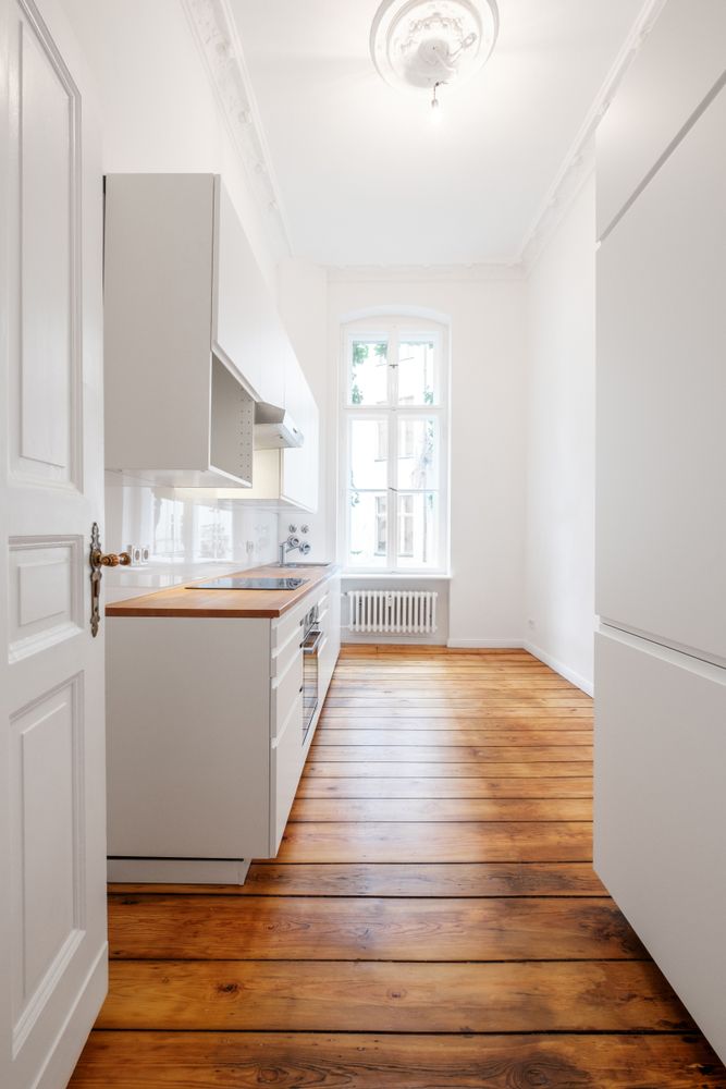 A Long Hallway Leading to a Kitchen With Wooden Floors and White Cabinets — Bathurst Bathroom Solutions In Eglinton, NSW