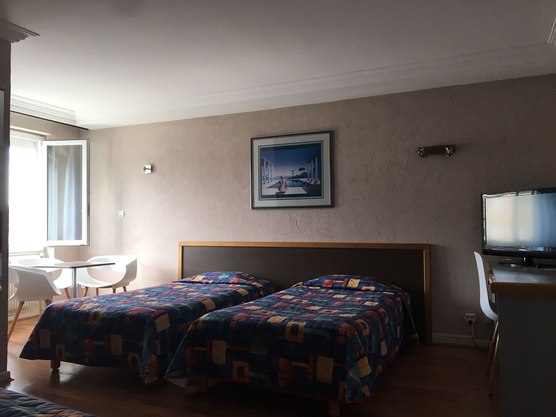 Chambre d'hôtel avec deux lits jumeaux, un bureau, une télévision et une fenêtre ouverte sur la gauche.