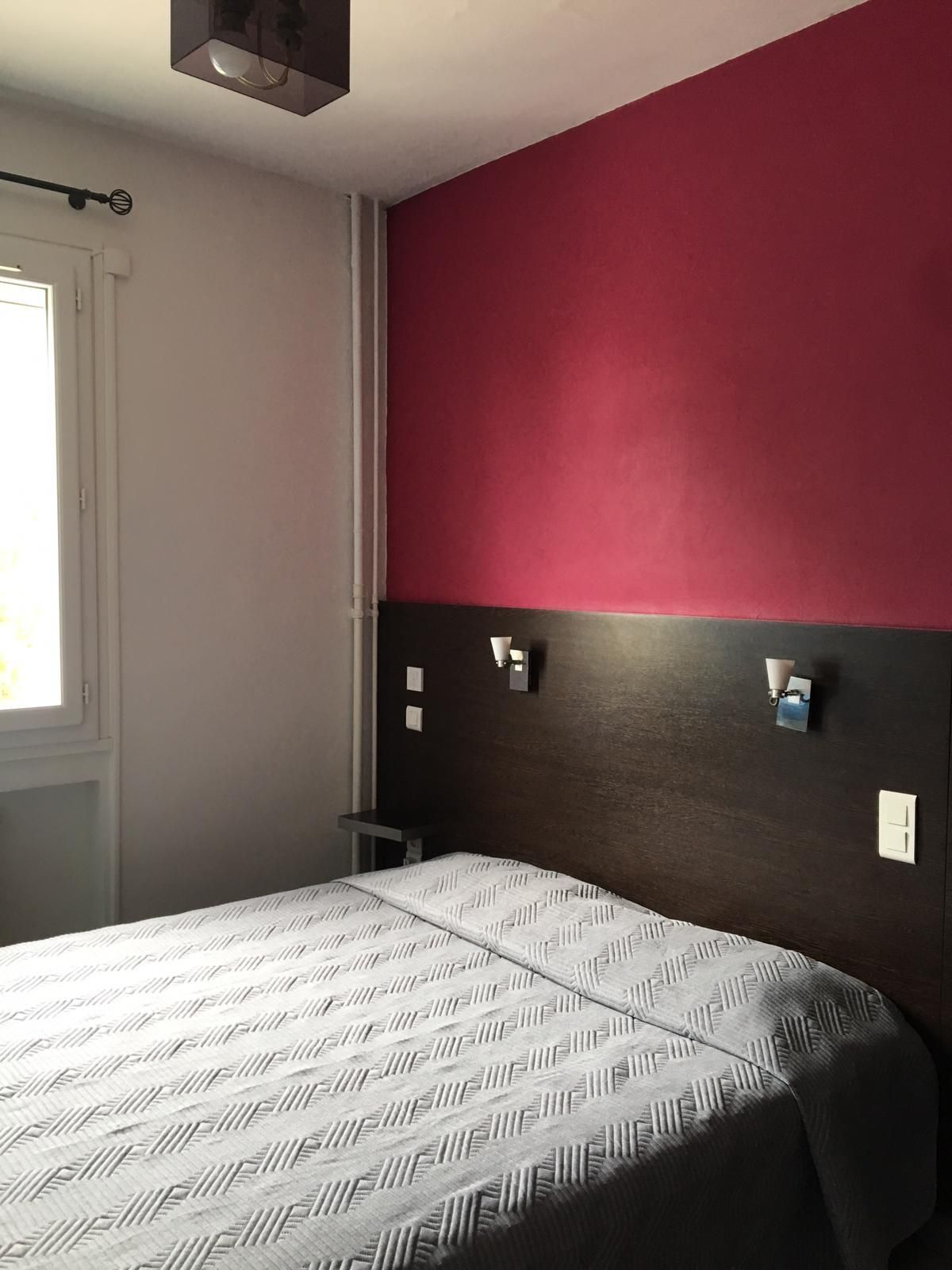 Chambre avec un mur d'accent rose, une tête de lit foncée et un lit près d'une fenêtre.