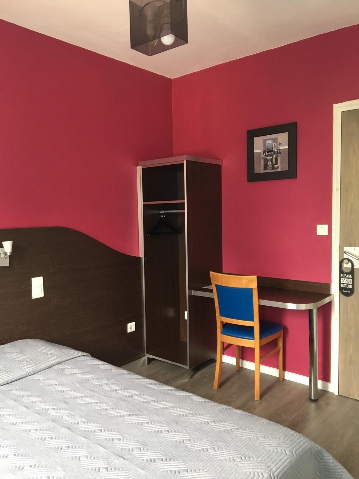 Chambre avec murs rouges, un lit, un bureau, une chaise, une armoire et des tableaux.