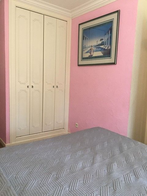 Chambre rose avec armoire blanche, tableaux encadrés et lit au premier plan