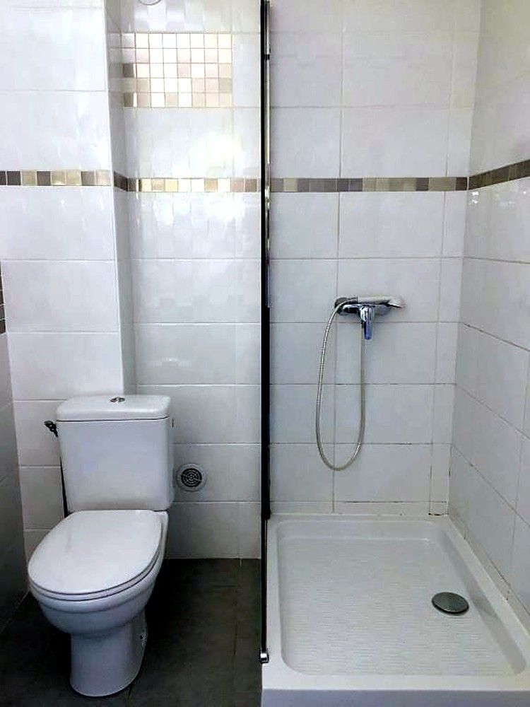 Petite salle de bains avec toilettes et cabine de douche, murs et sol carrelés de blanc.