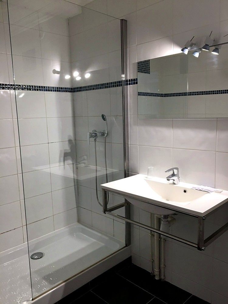 Salle de bains moderne blanche avec douche en verre, murs carrelés et lavabo suspendu avec meuble-miroir
