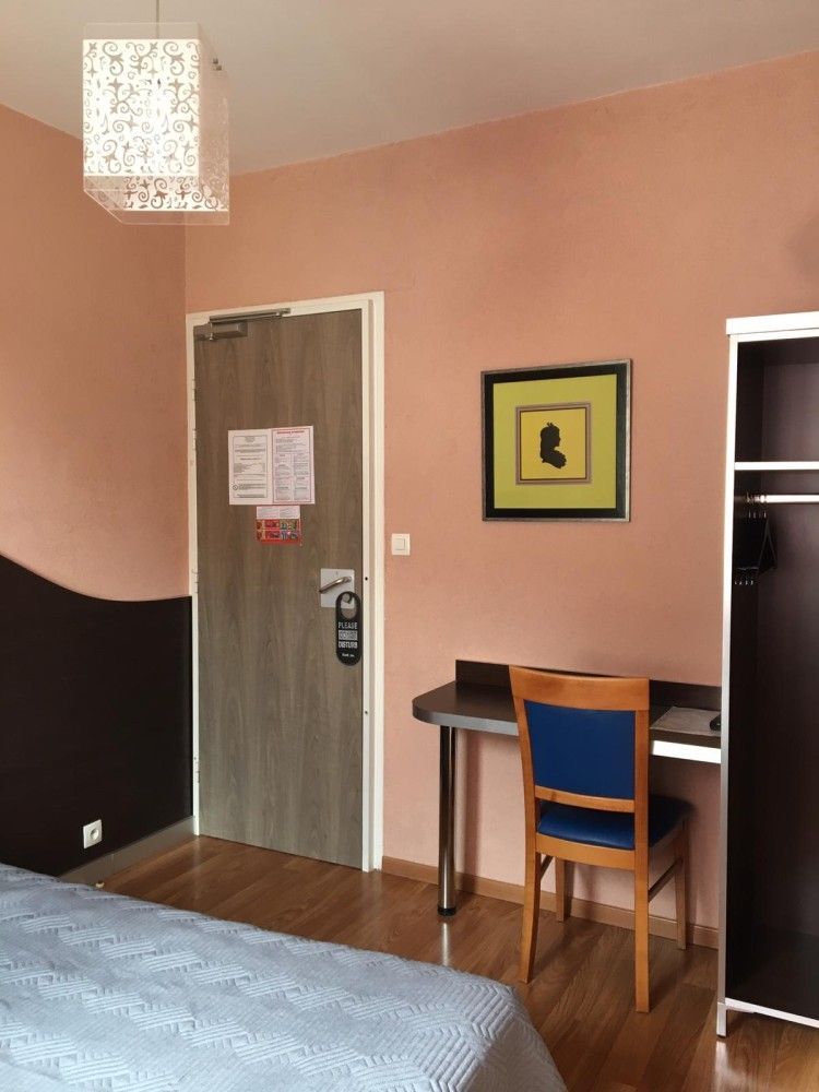 Petite pièce avec un bureau, une chaise, une armoire et une porte sur des murs roses avec un panneau inférieur foncé.
