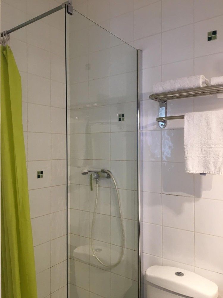 Salle de bains carrelée avec cabine de douche en verre, étagère murale avec porte-serviettes et toilettes blanches