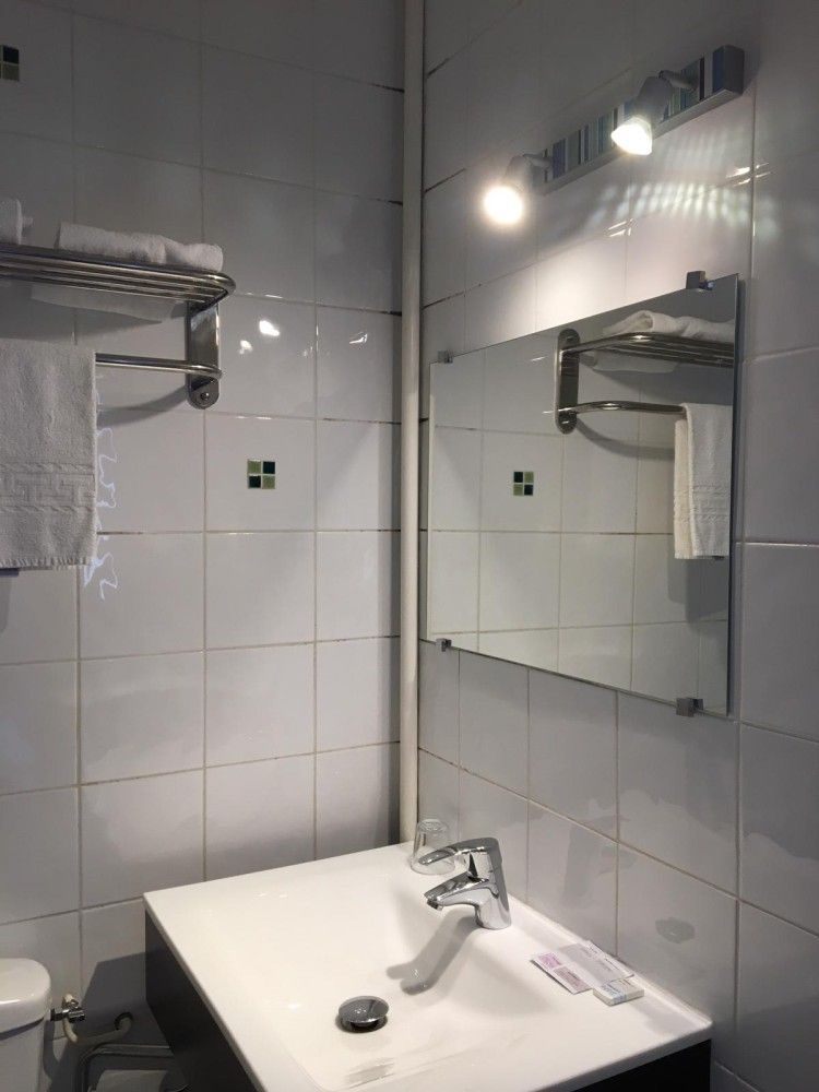 Petit lavabo de salle de bain avec miroir, applique murale, porte-serviettes et murs carrelés.