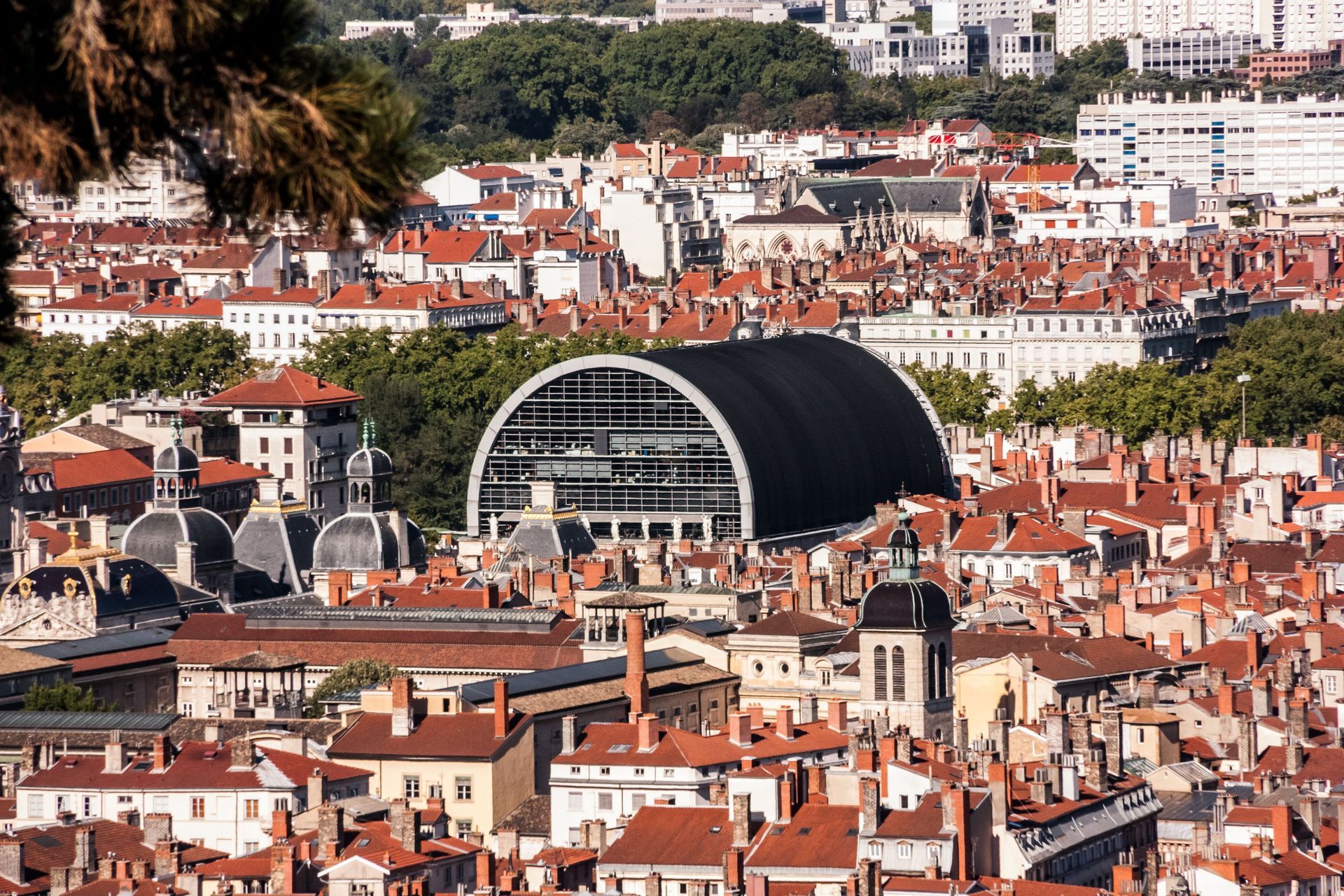 Vue panoramique d'une ville aux toits de tuiles rouges et d'un grand bâtiment voûté au toit noir en son centre