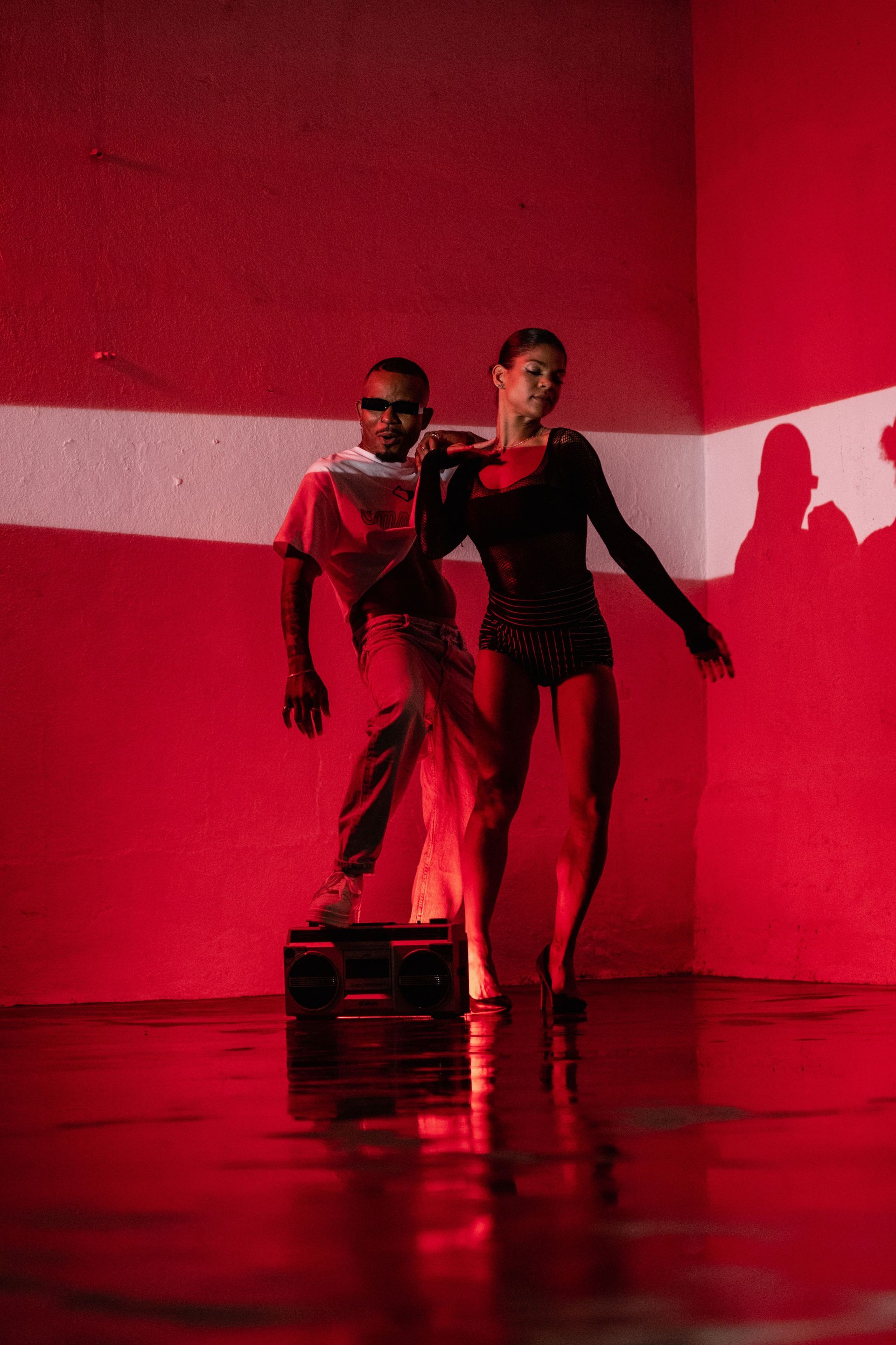 Deux danseurs, baignés d'une lumière rouge, évoluent sur une scène brillante devant un mur rouge et blanc.
