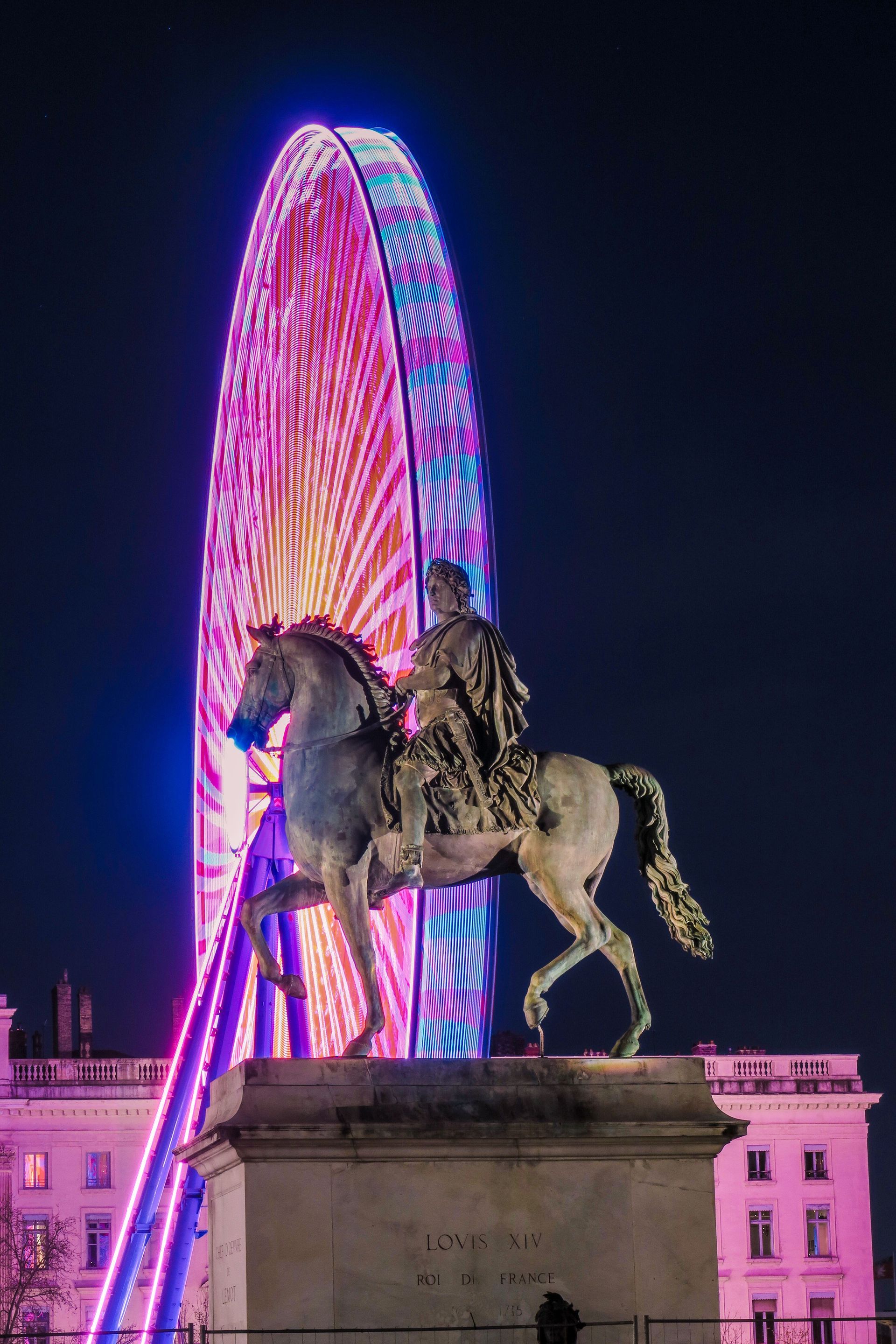 Statue équestre se détachant en silhouette devant une grande roue illuminée la nuit