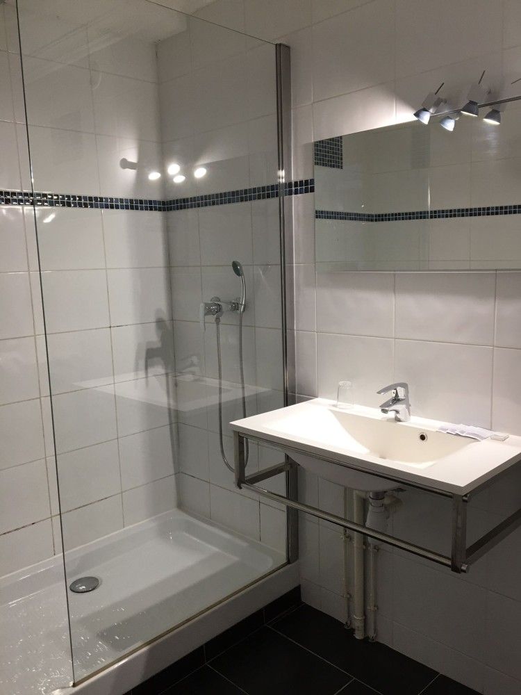 Salle de bains moderne avec douche en verre, carrelage blanc, lavabo et meuble-lavabo avec miroir.