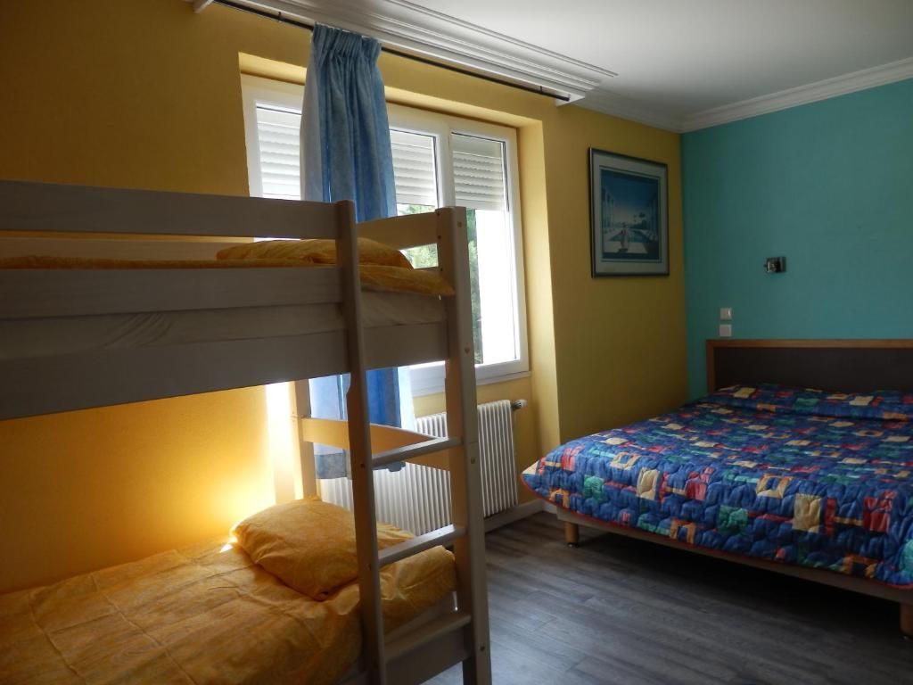 Chambre avec lit superposé, lit simple, murs bleus et lumière du soleil entrant par la fenêtre