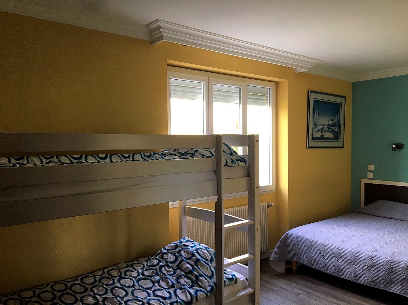 Chambre avec lit superposé, lit simple, murs jaunes et turquoise, et une fenêtre entre les lits