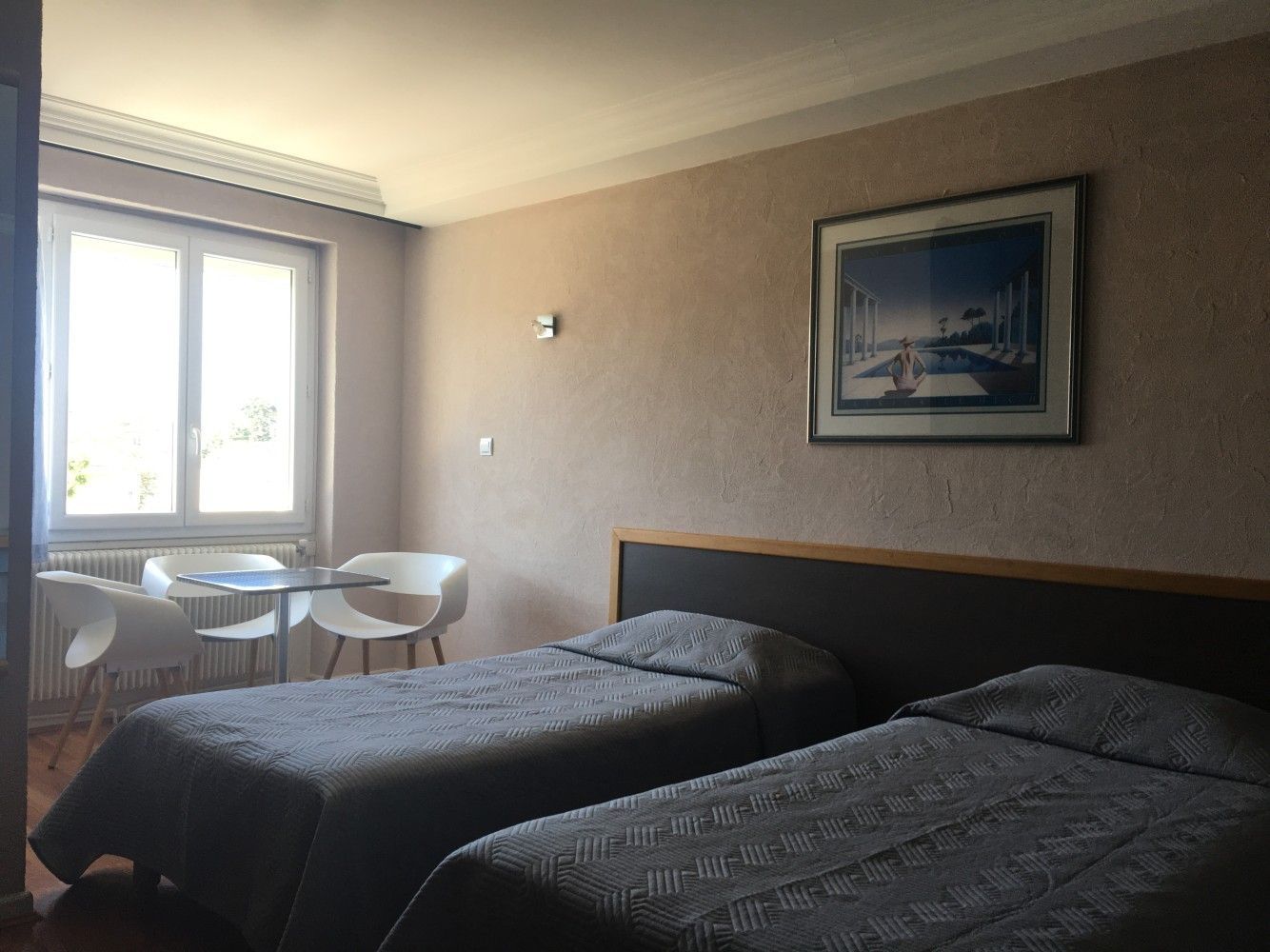 Chambre d'hôtel avec deux lits jumeaux, une petite table près de la fenêtre et des tableaux encadrés.