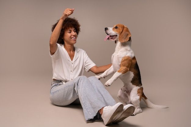 Person sitting on the floor with a beagle, both looking happy against a plain beige background