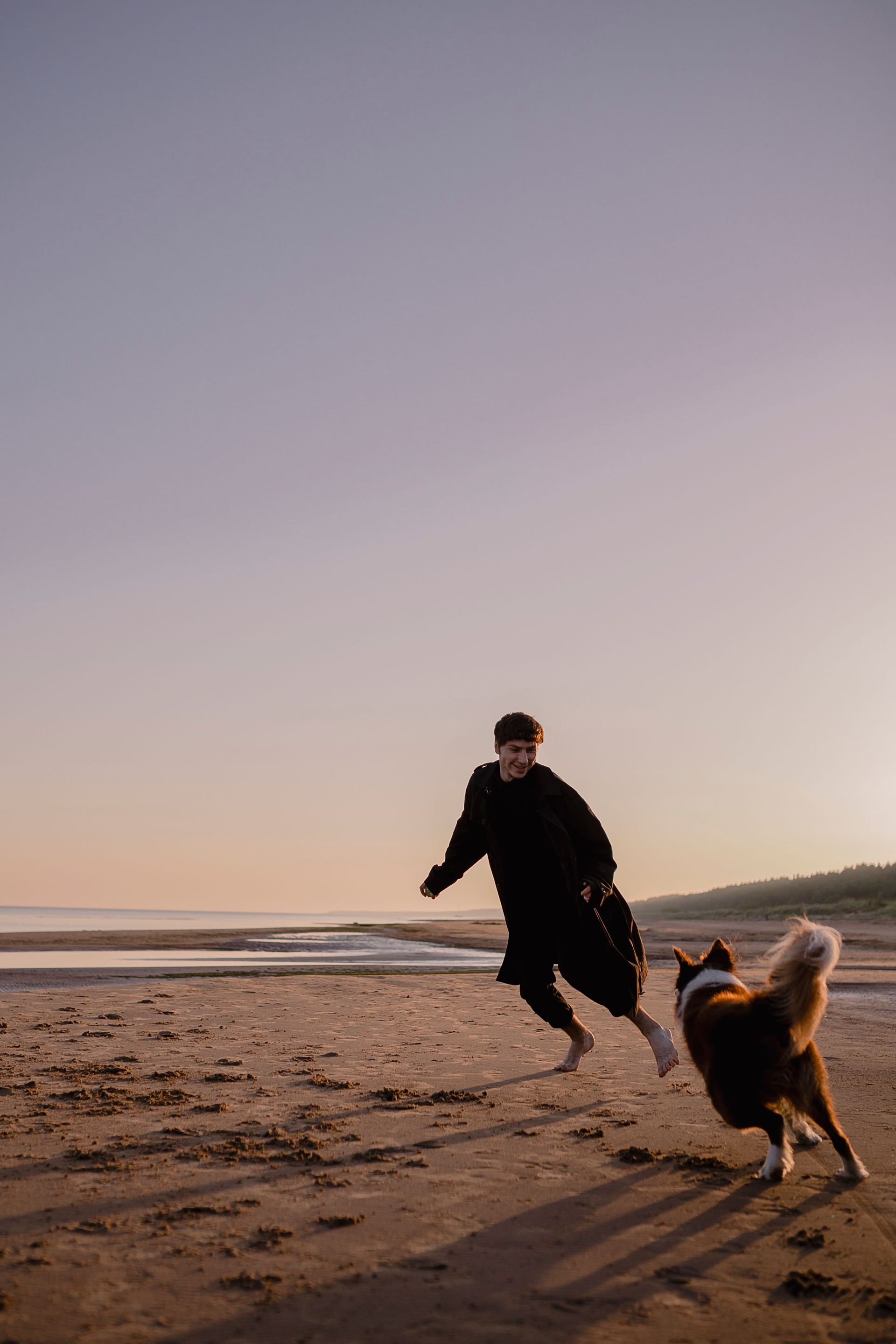 Person and dog running on a beach at sunset