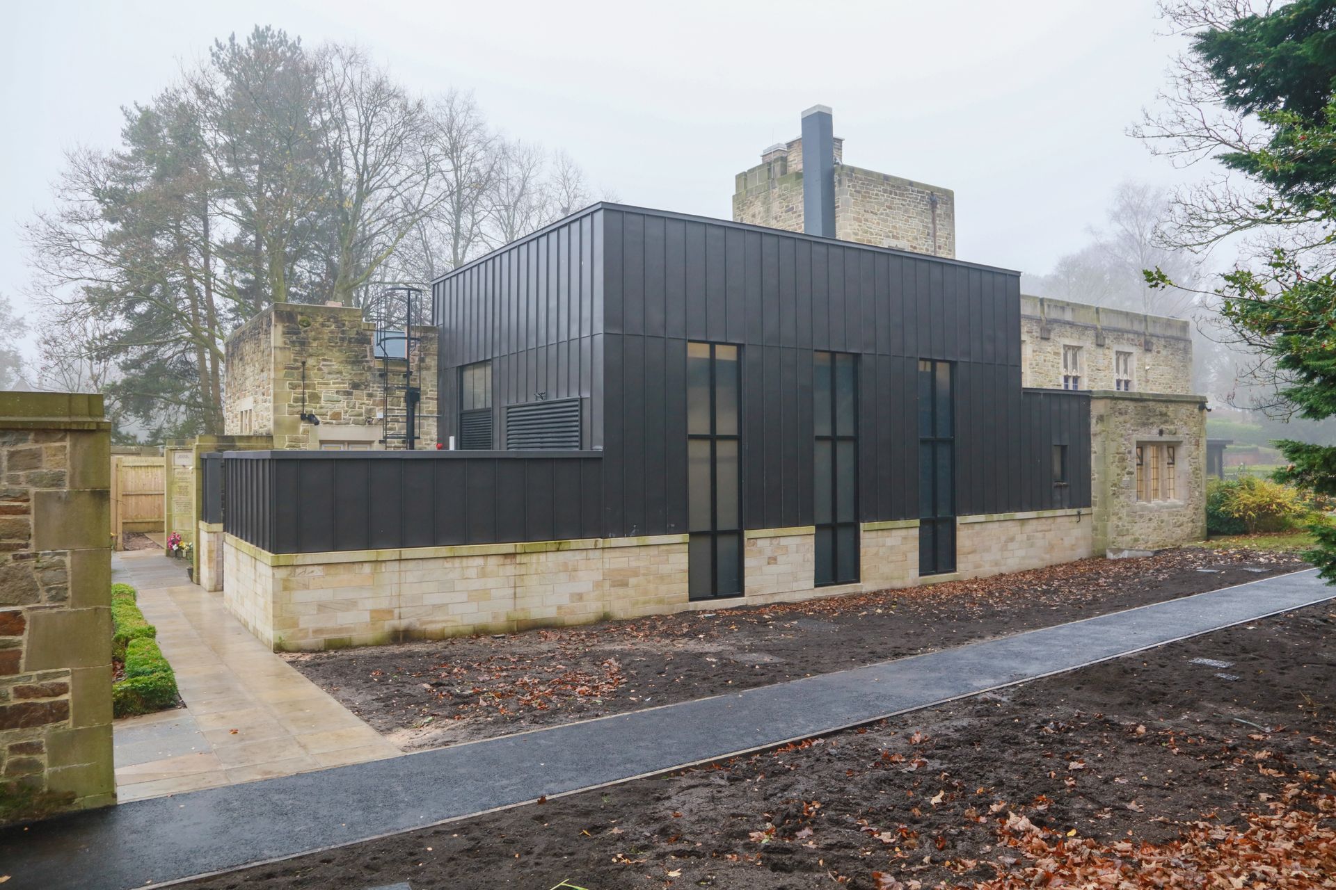 A large building with a lot of windows is surrounded by trees on a foggy day.