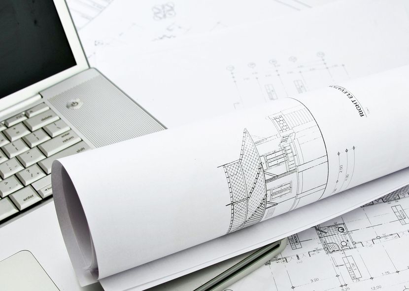 A drawing of a building is rolled up next to a laptop