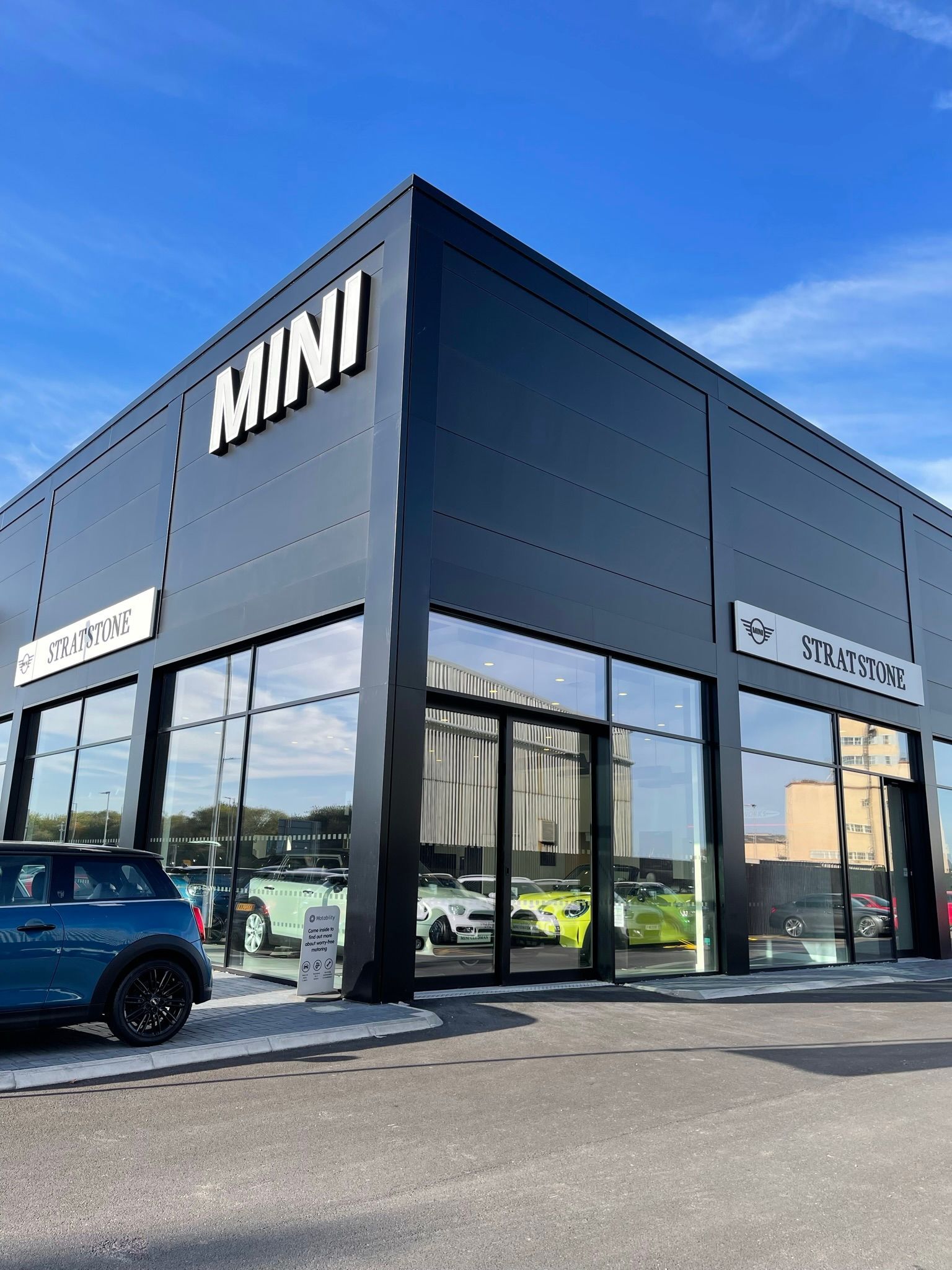 A blue mini cooper is parked in front of a mini car dealership.