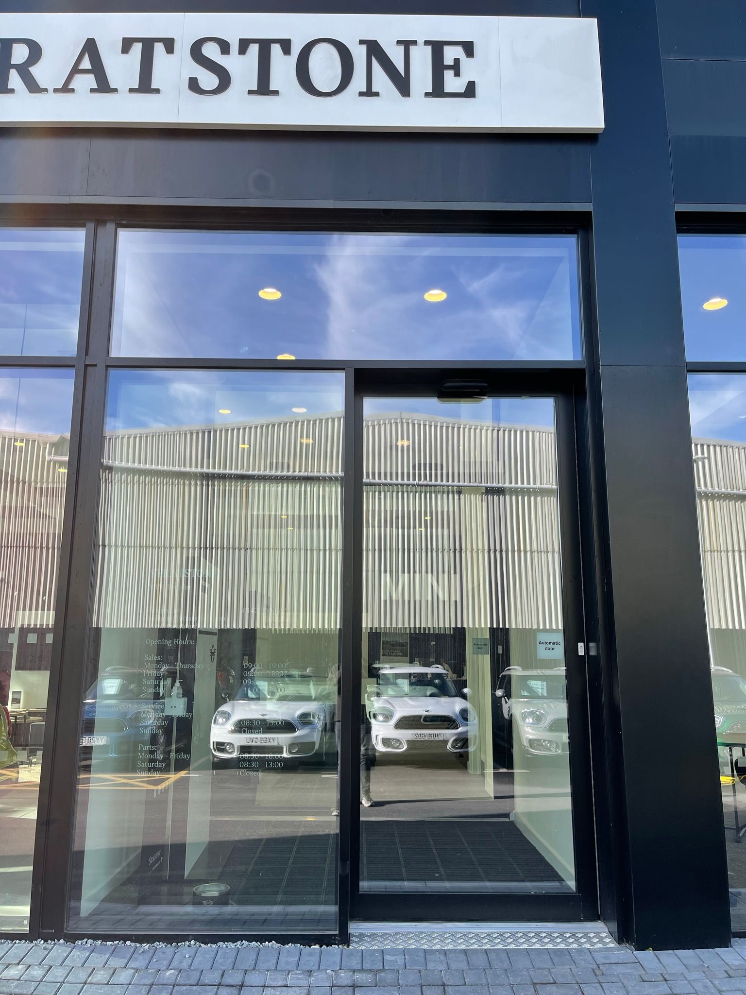 The front door of a car dealership with cars parked in front of it.