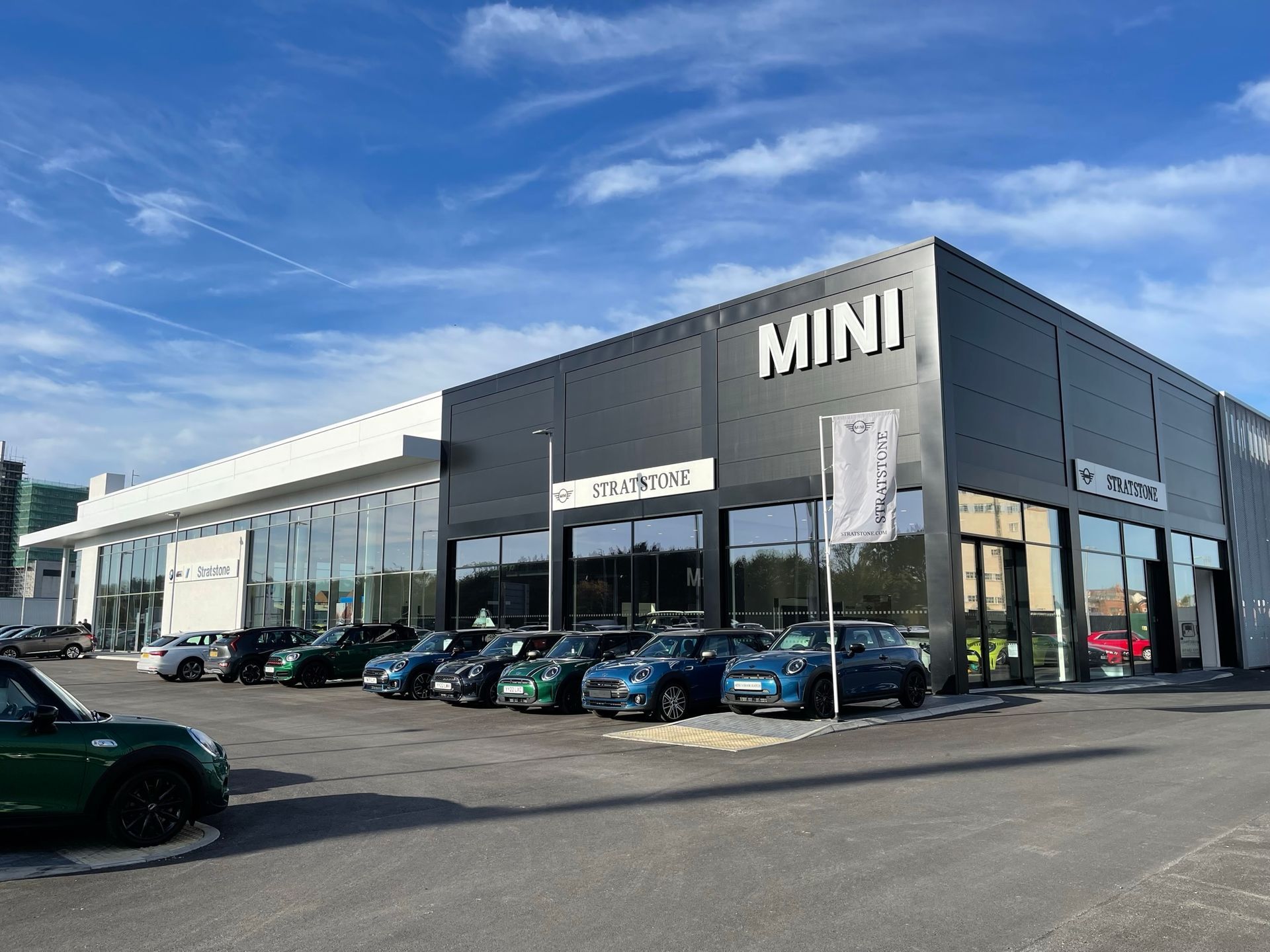 A row of cars are parked in front of a mini car dealership.